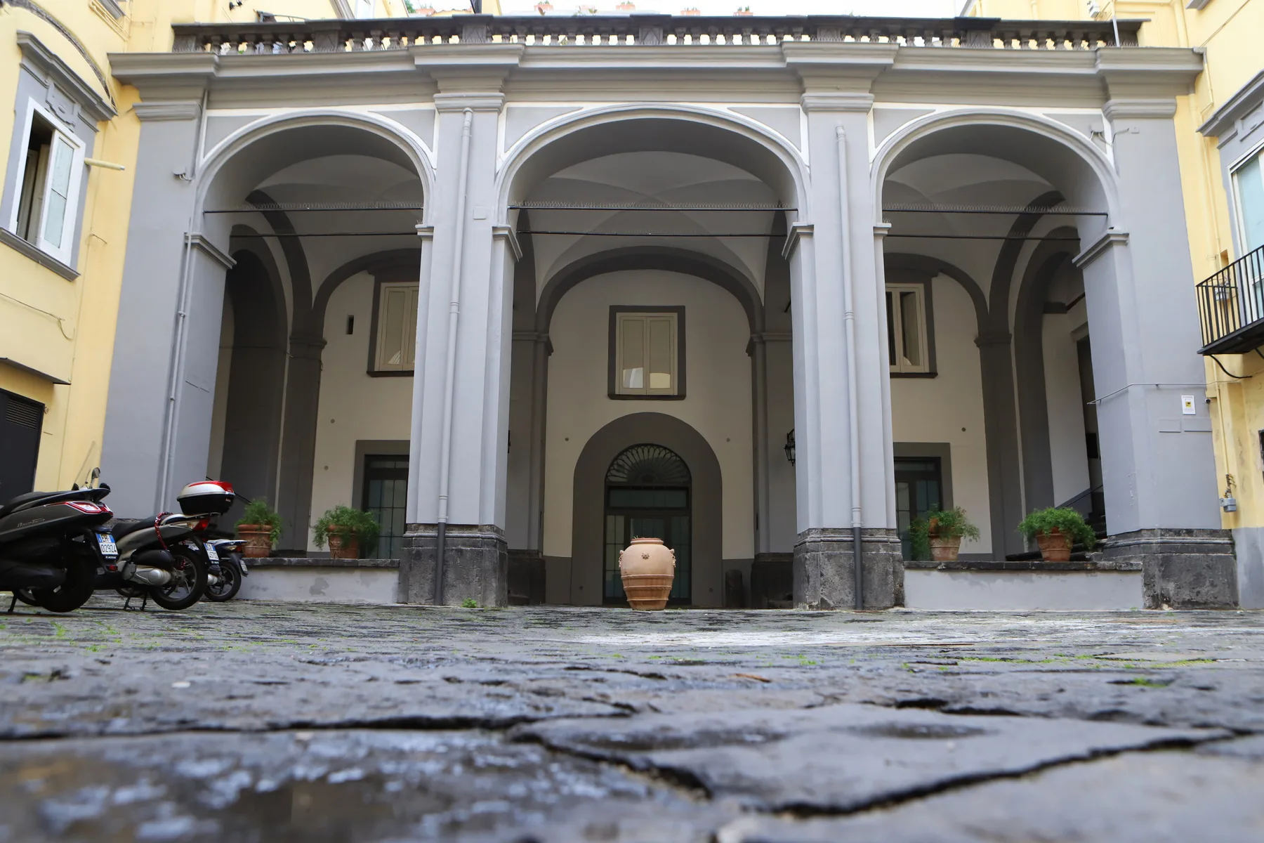 Una fachada de patio con tres grandes arcos y adoquines en primer plano.