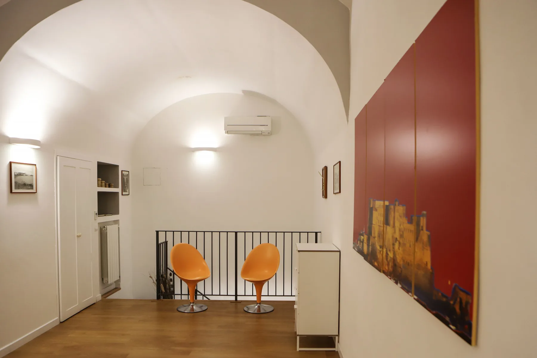 Un pasillo interior luminoso con techos arqueados, asientos naranjas y obras de arte.
