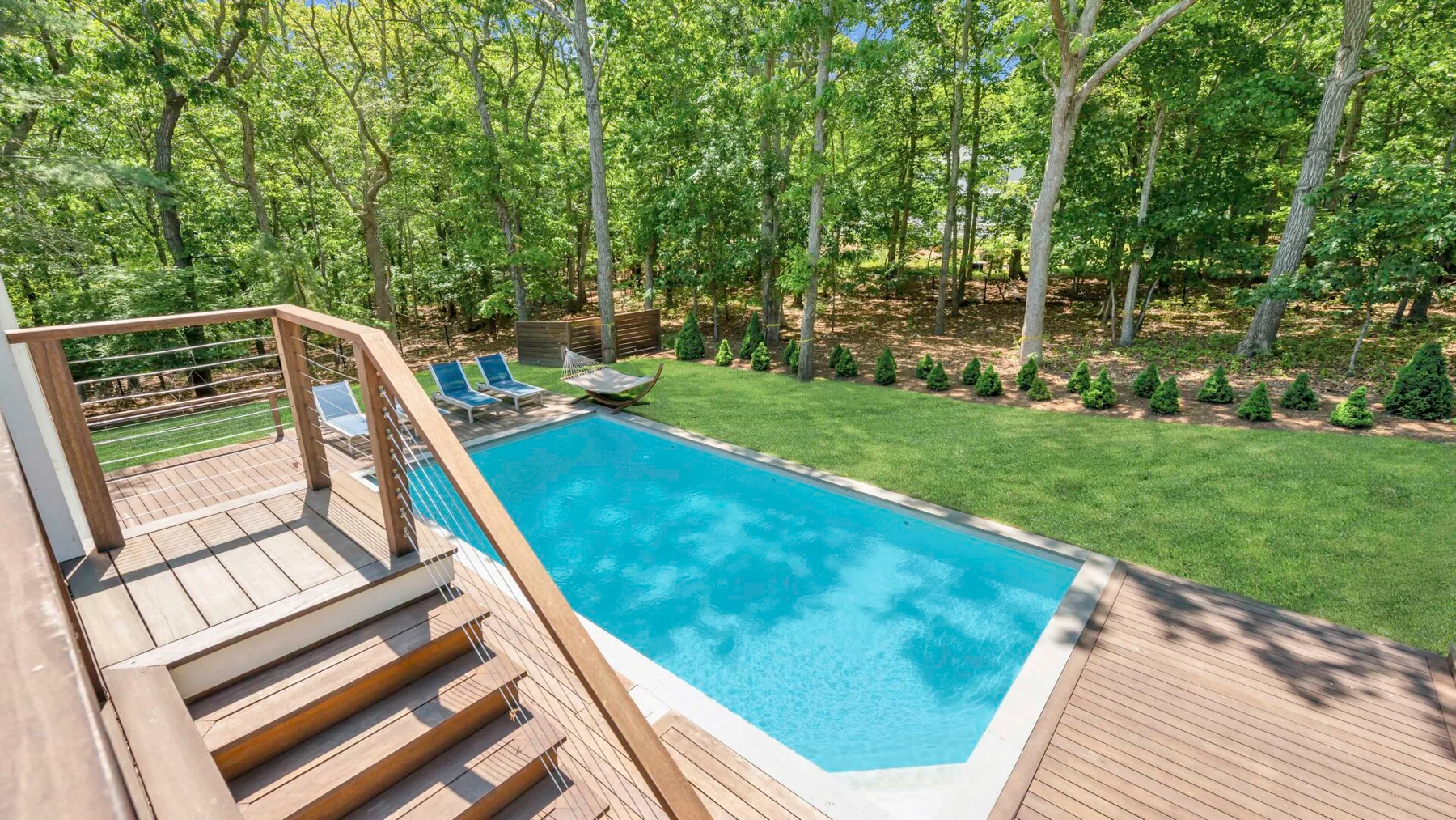 Una piscina al aire libre está junto a una terraza de madera, rodeada de árboles.