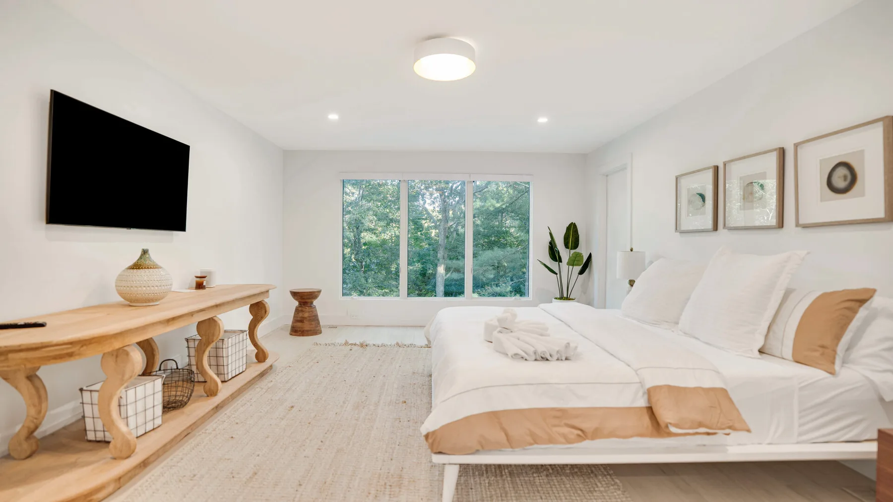 Un dormitorio luminoso con una cama grande frente a una ventana con vistas a los árboles.