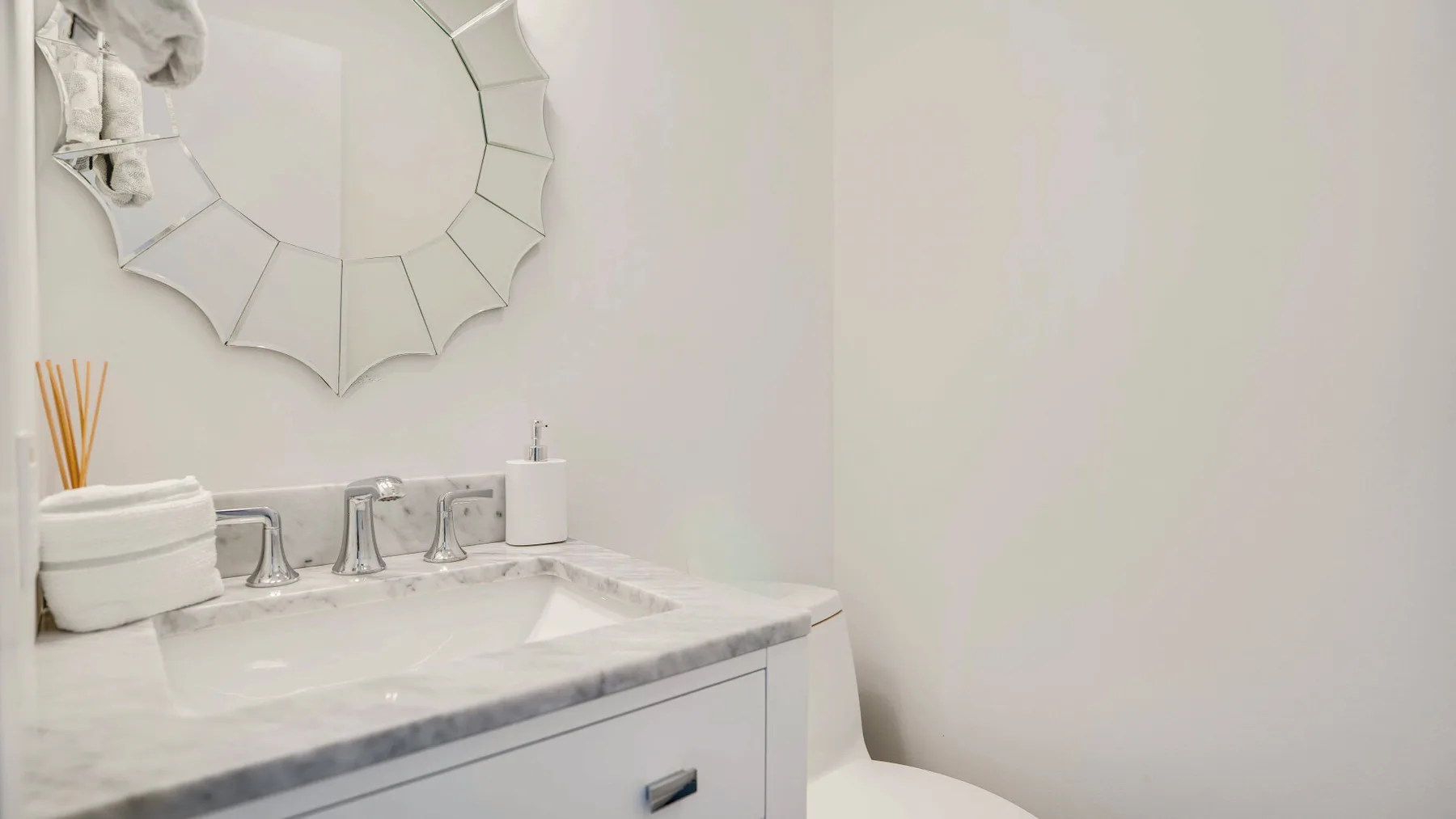 Un tocador de baño con lavabo blanco y un espejo decorativo en la pared.