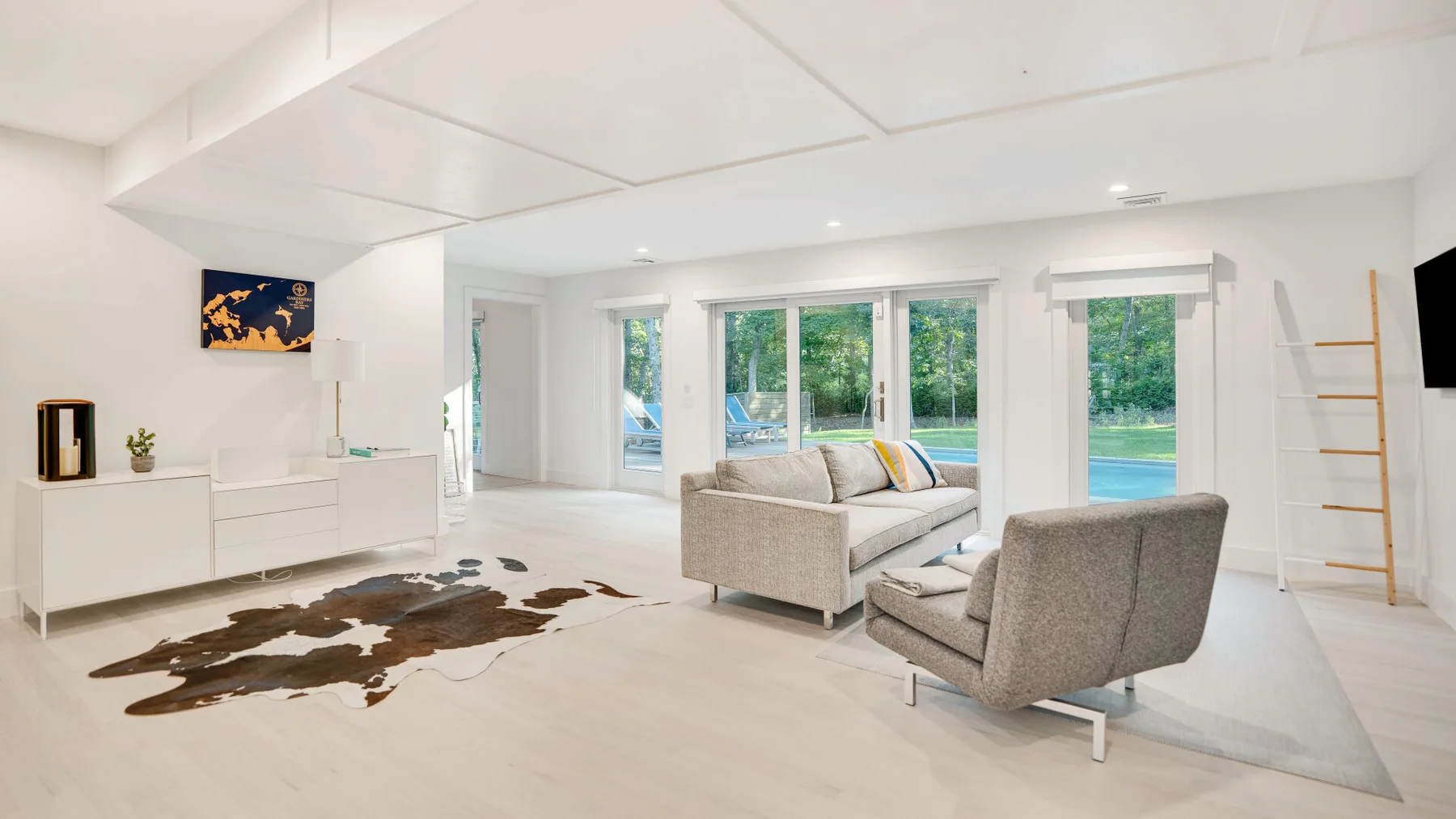 Una luminosa sala de estar con asientos frente a grandes ventanales con vista a una piscina.