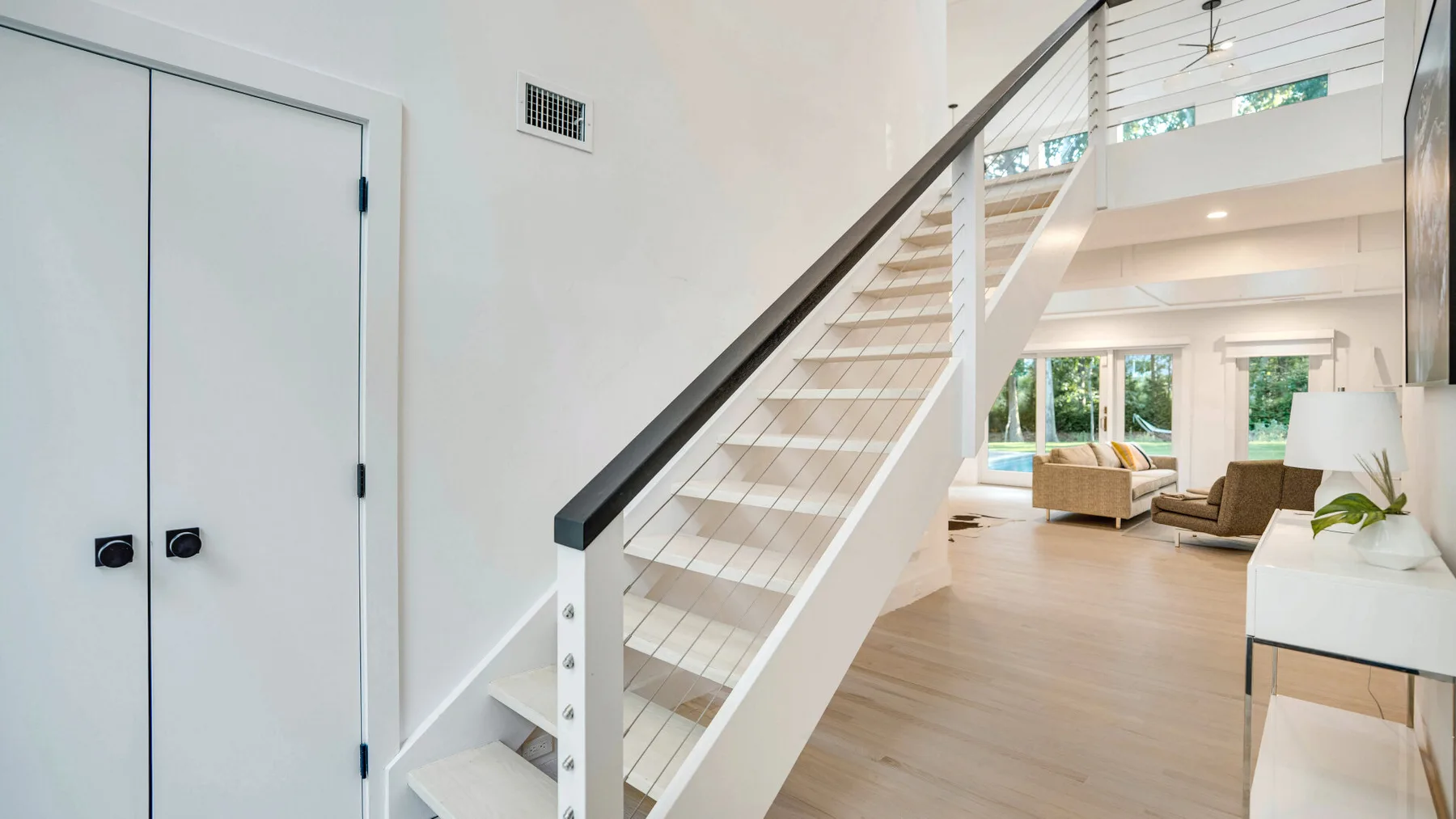 Un interior luminoso muestra una escalera junto a una sala de estar con asientos.