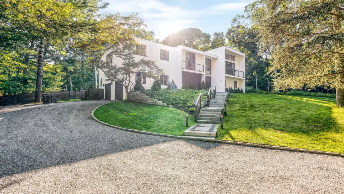 Una casa blanca de estilo moderno se alza junto a un camino curvo y un césped verde.