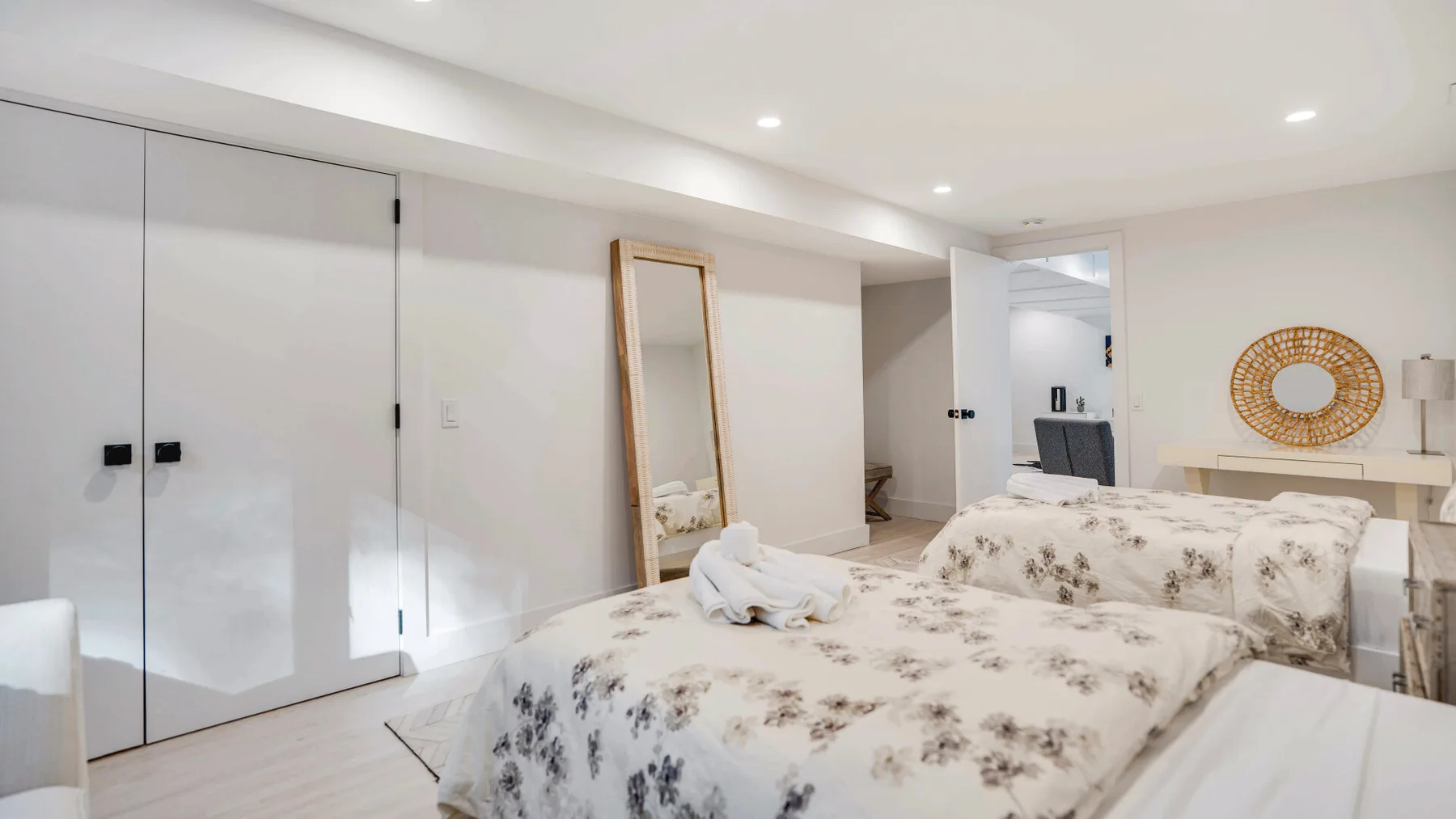 Un dormitorio con una colcha floral y un espejo de cuerpo entero apoyado contra la pared.