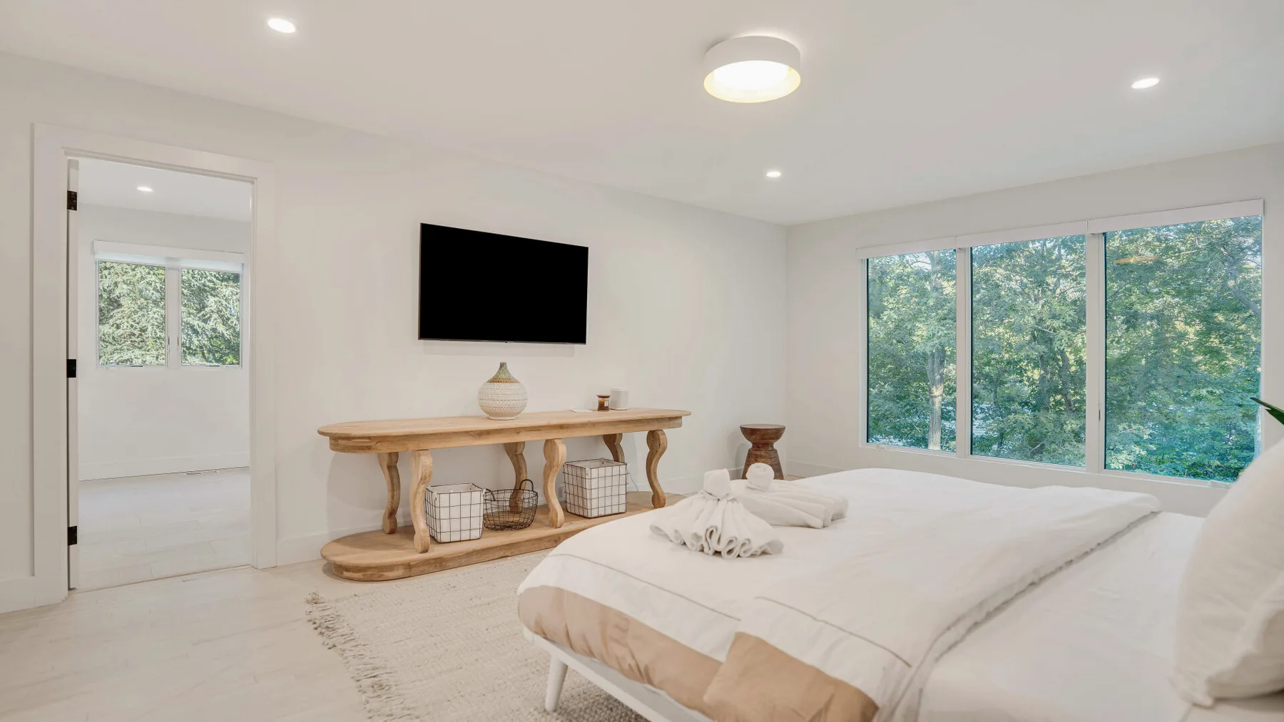 Un dormitorio luminoso con una cama bien arreglada y grandes ventanas con vistas a la vegetación.