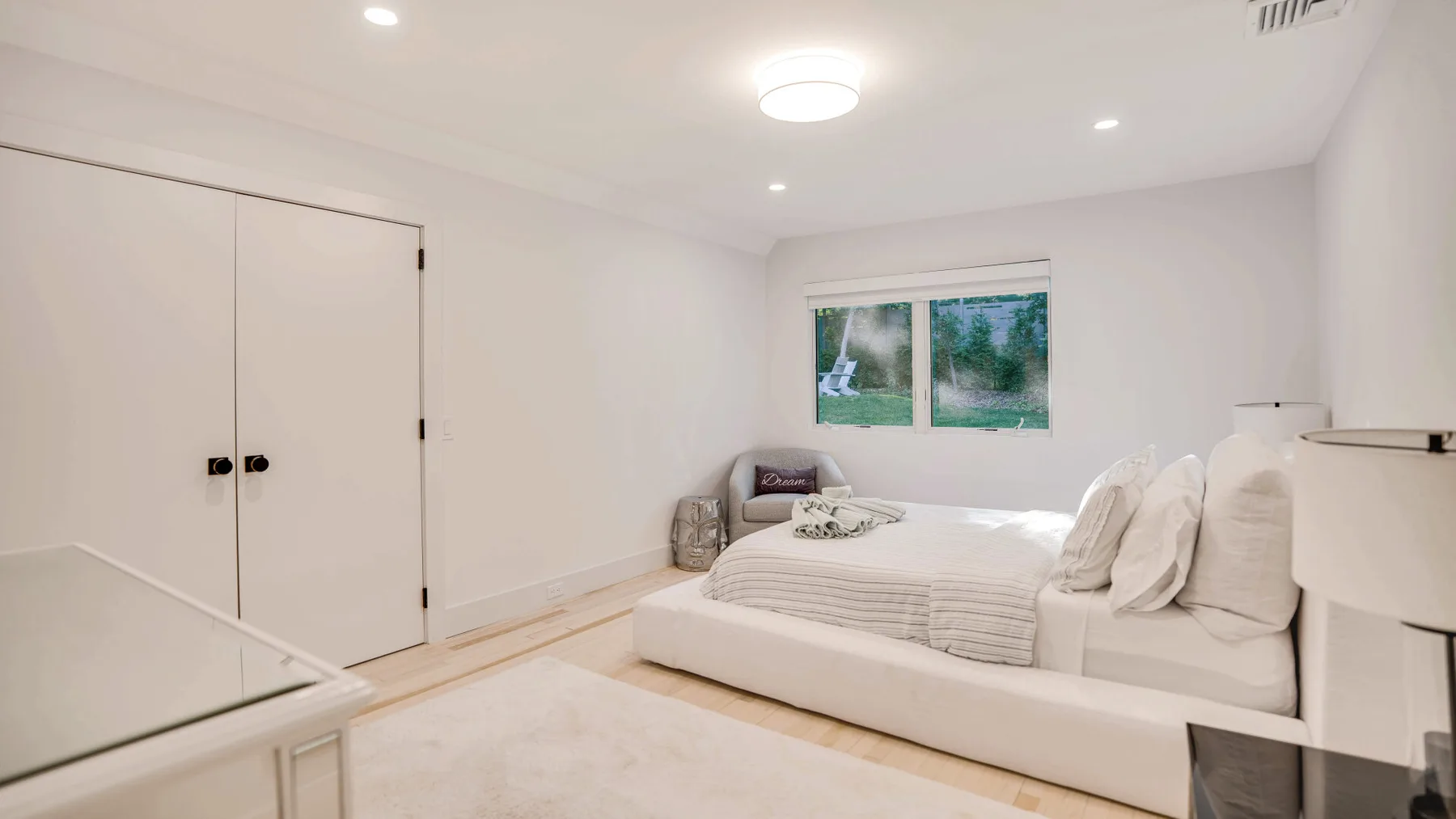 Un dormitorio luminoso con una cama baja, ropa de cama blanca y una ventana.