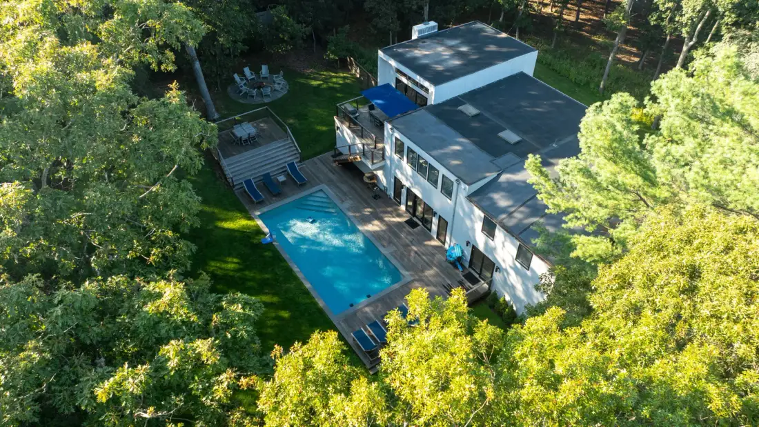 Vista aérea de una casa y una piscina rodeadas de árboles.