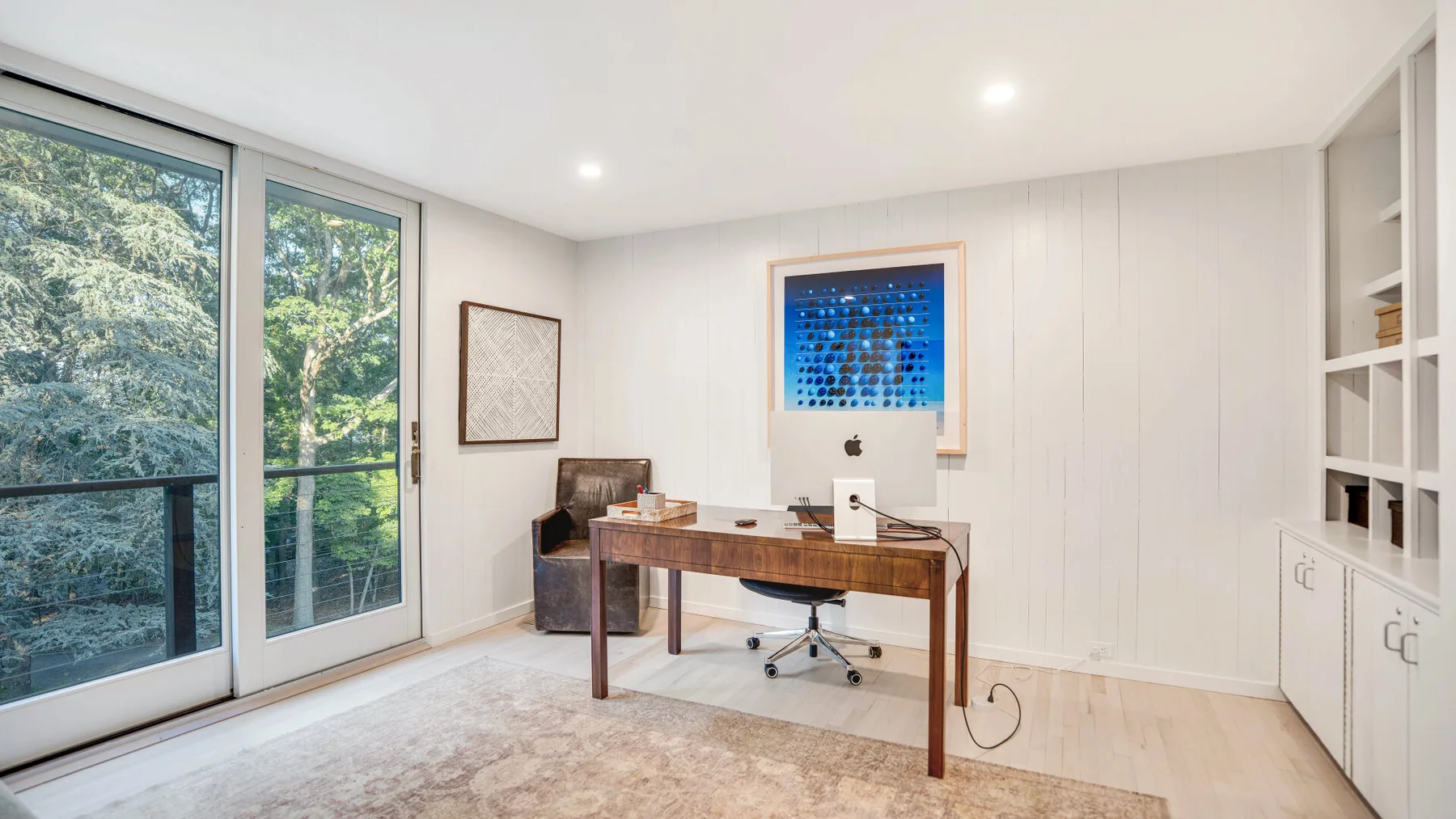 Un estudio luminoso con un escritorio de madera y grandes ventanas que dan a los árboles.