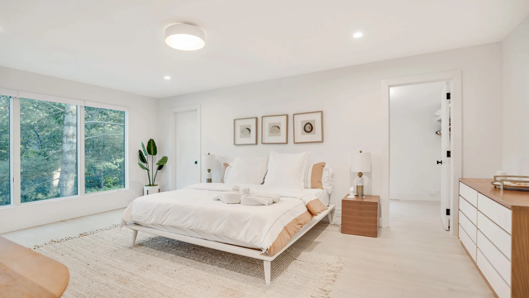 Un dormitorio luminoso con una cama bien tendida junto a grandes ventanas.