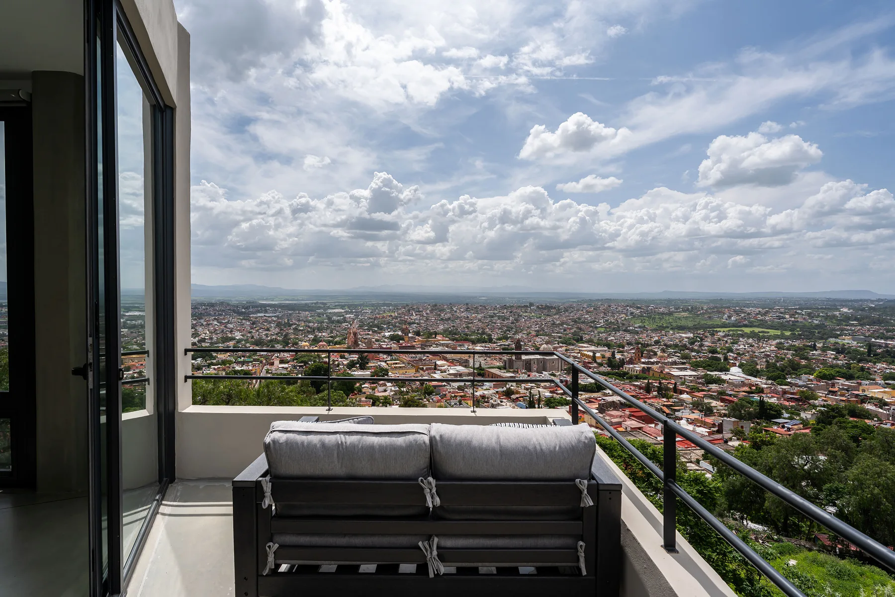 A balcony seating area overlooks a wide cityscape beneath a cloudy sky.