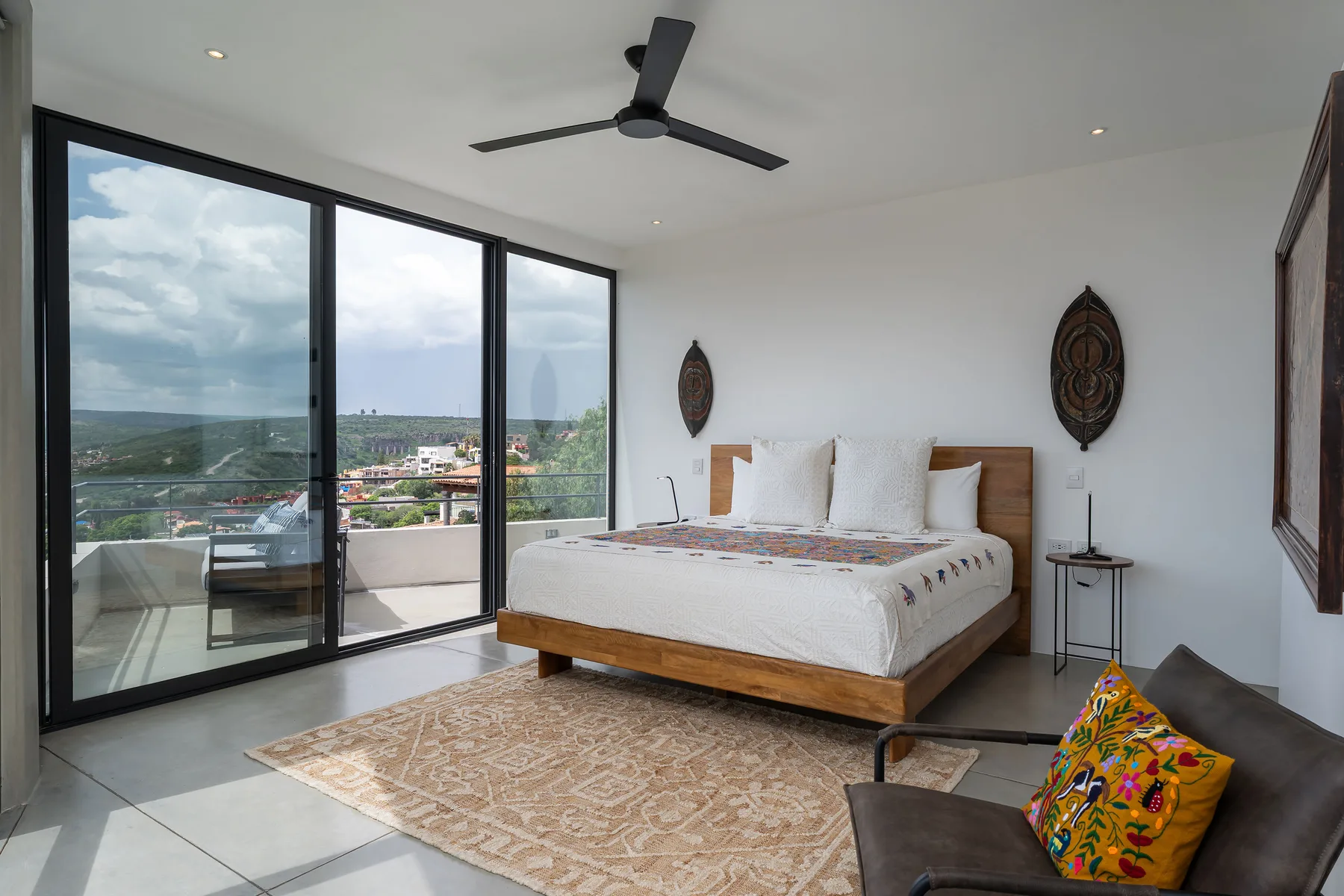 A bright bedroom with a wooden bed and large glass doors overlooking the landscape.