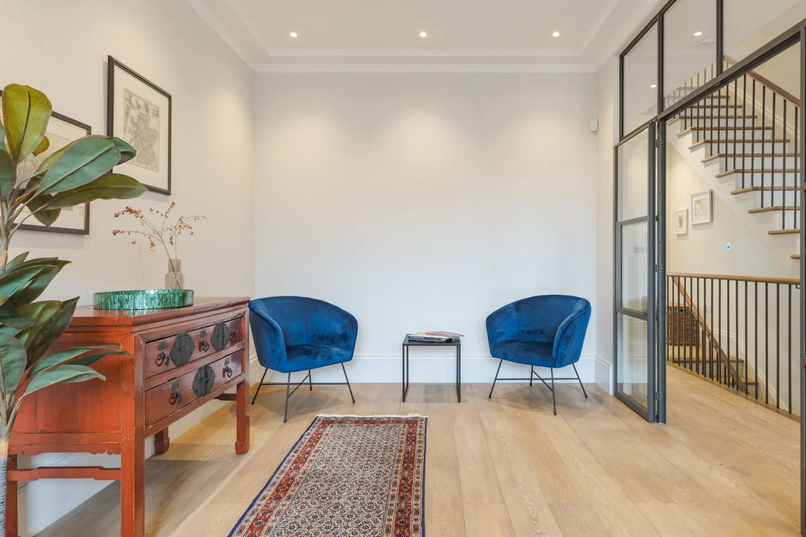 Una luminosa zona de estar con asientos azules, un aparador de madera y una mampara de vidrio.