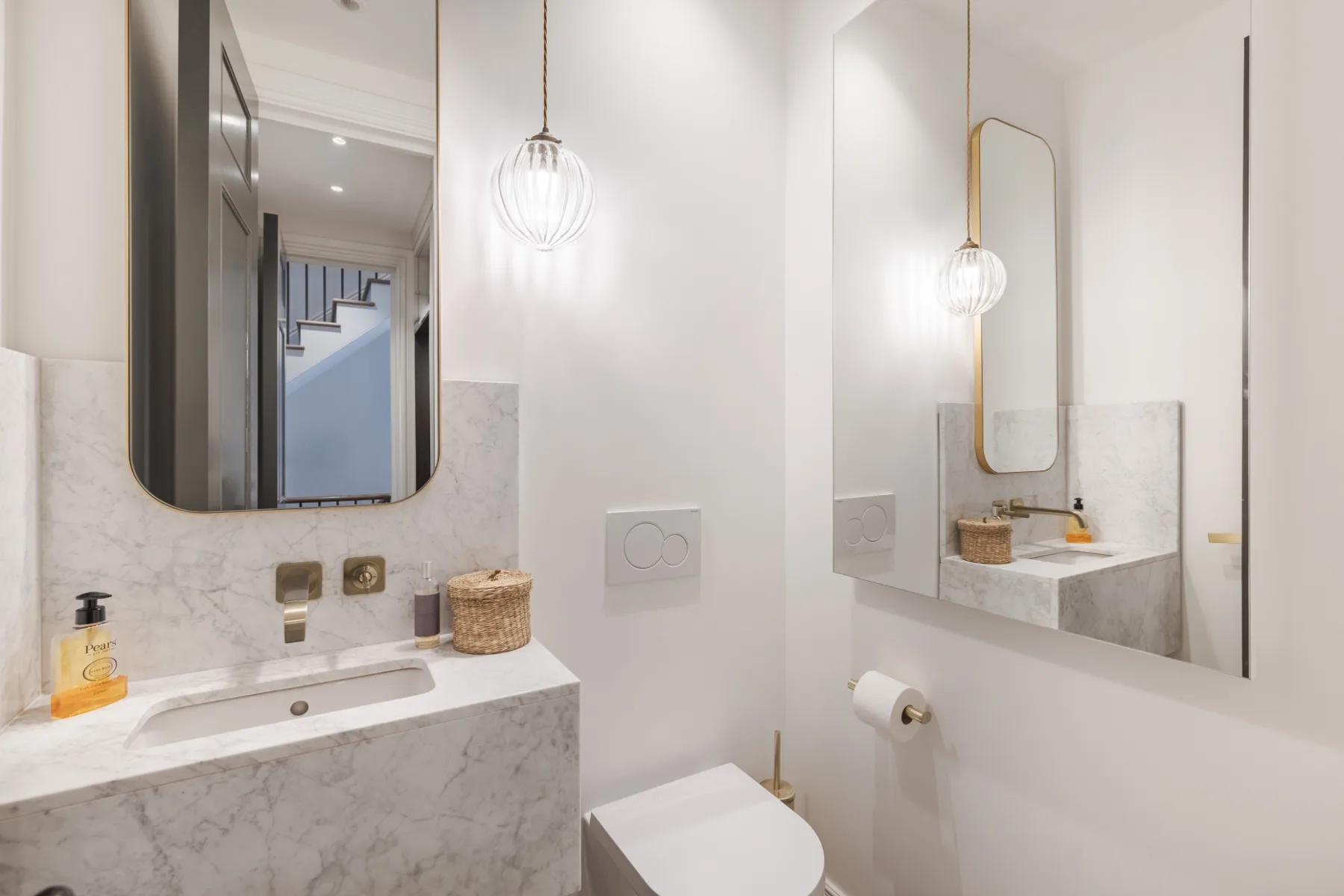 Un baño luminoso con lavabo de mármol, espejos en la pared e inodoro.