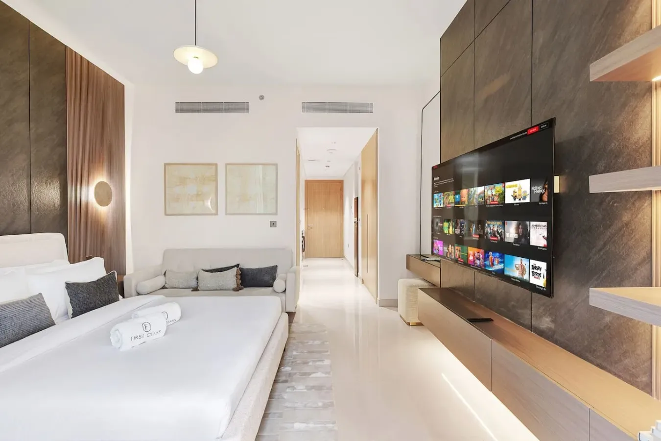 Un dormitorio luminoso con cama, asientos y un televisor junto a la pared.