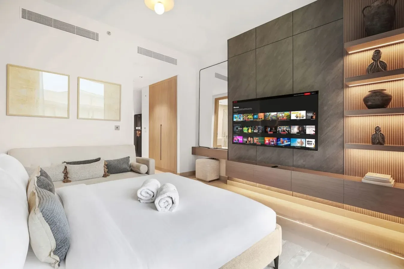 Un dormitorio con una cama frente a un televisor montado en la pared y estanterías empotradas.