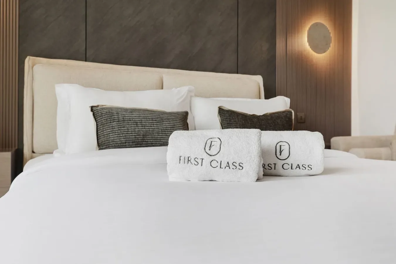 Una cama bien tendida con varias almohadas y dos toallas dobladas.