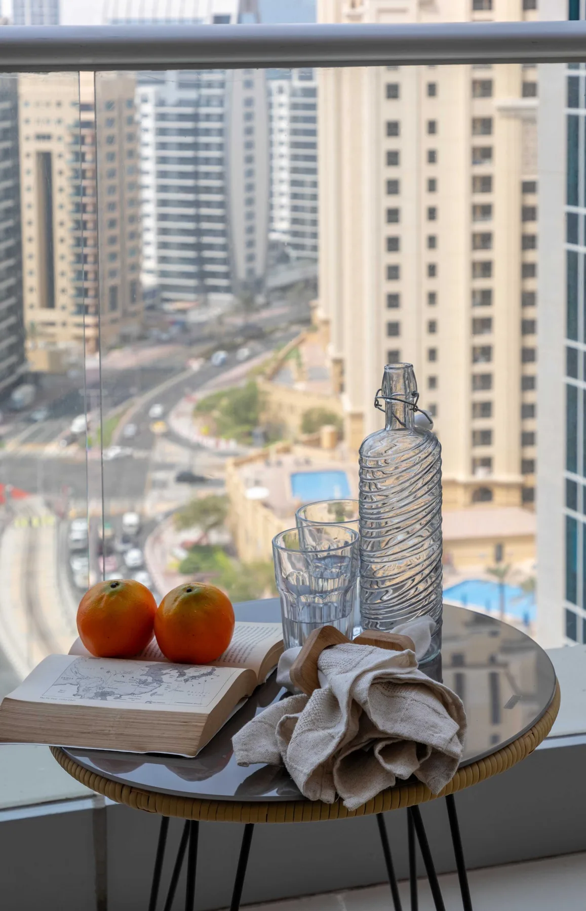 Una mesa pequeña junto a una ventana tiene fruta, una botella de agua y vasos.