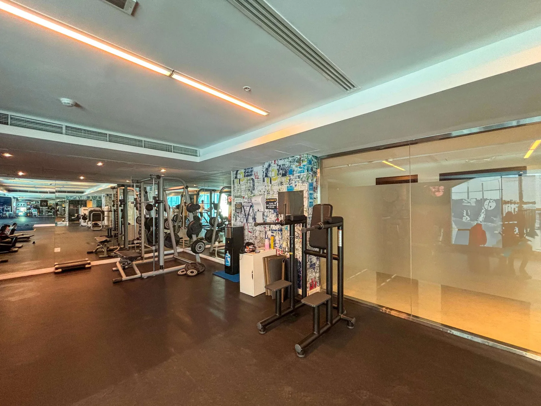 Un gimnasio con máquinas de ejercicio y una pared de vidrio junto a la zona de entrenamiento.