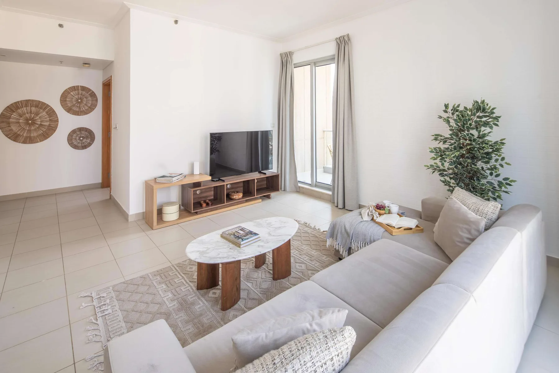 Una sala luminosa con televisor, asientos claros y una puerta de vidrio.