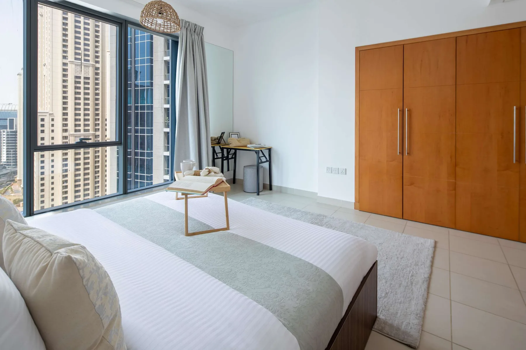 Un dormitorio luminoso con una cama, una ventana grande y un armario de madera.
