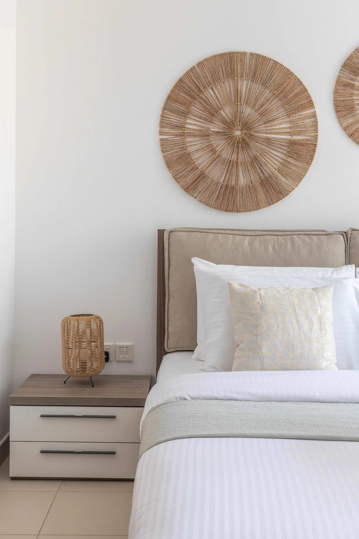 Un dormitorio con una cama bien tendida y decoración circular tejida en la pared.