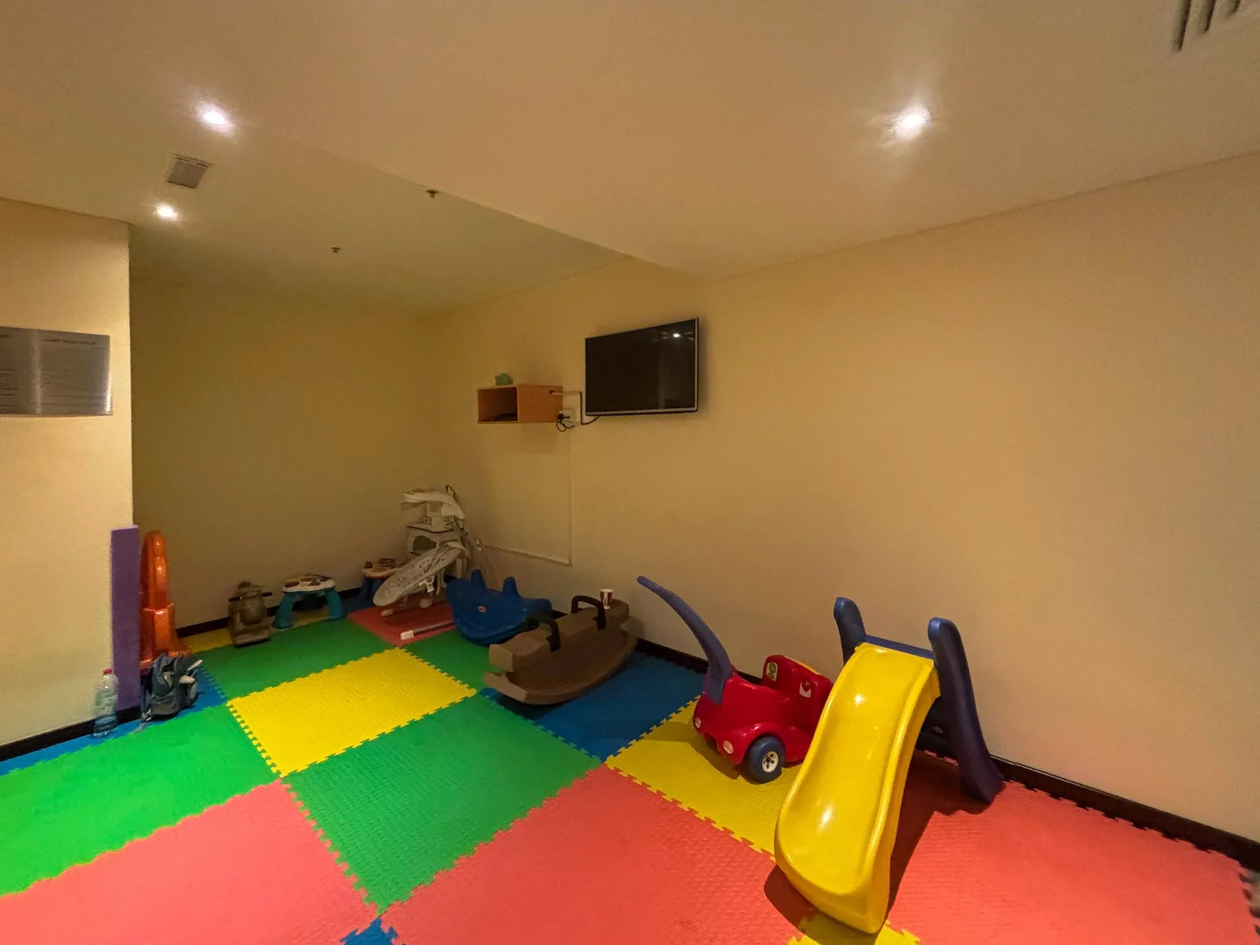 Una colorida zona de juegos interior con suelo de piezas acolchadas, juguetes y un tobogán pequeño.