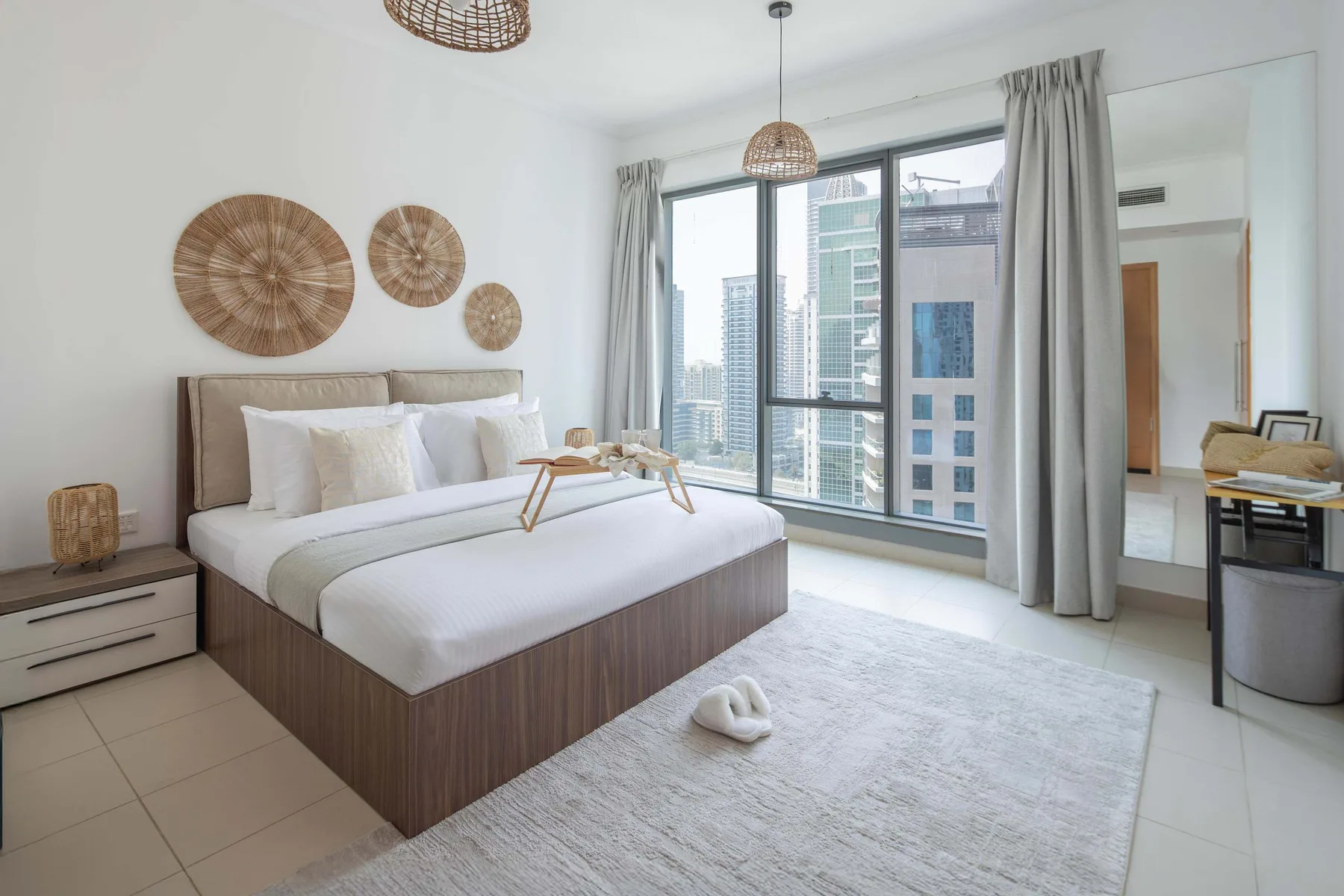 Un dormitorio luminoso con una cama bien tendida junto a grandes ventanas.