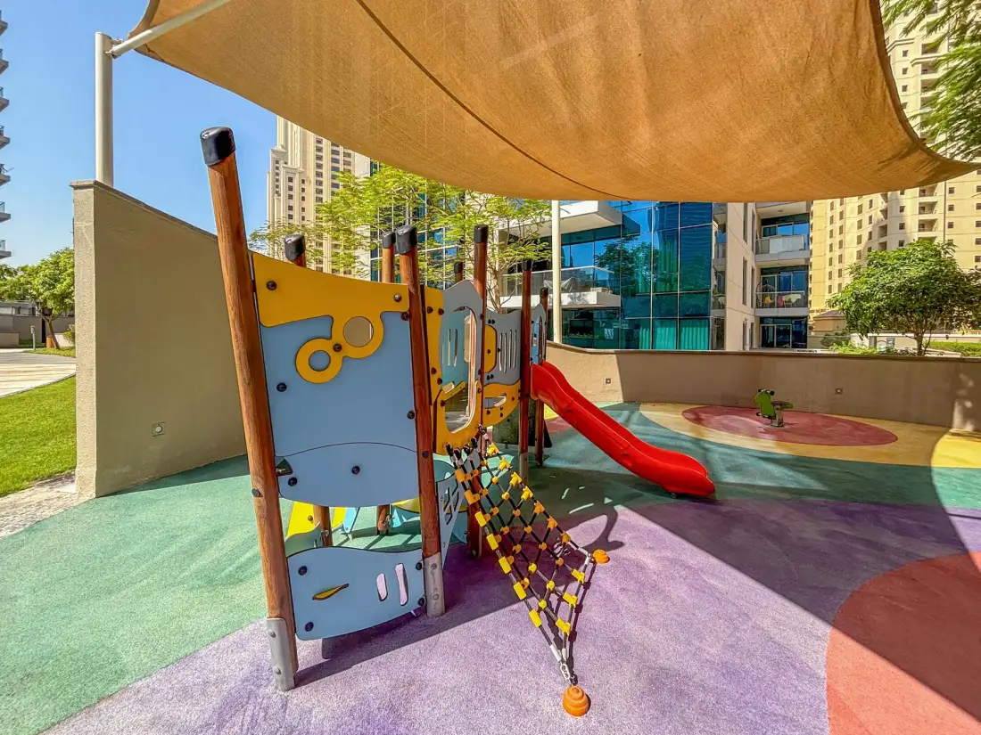 Un parque infantil al aire libre tiene paneles de escalada coloridos y un tobogán rojo.