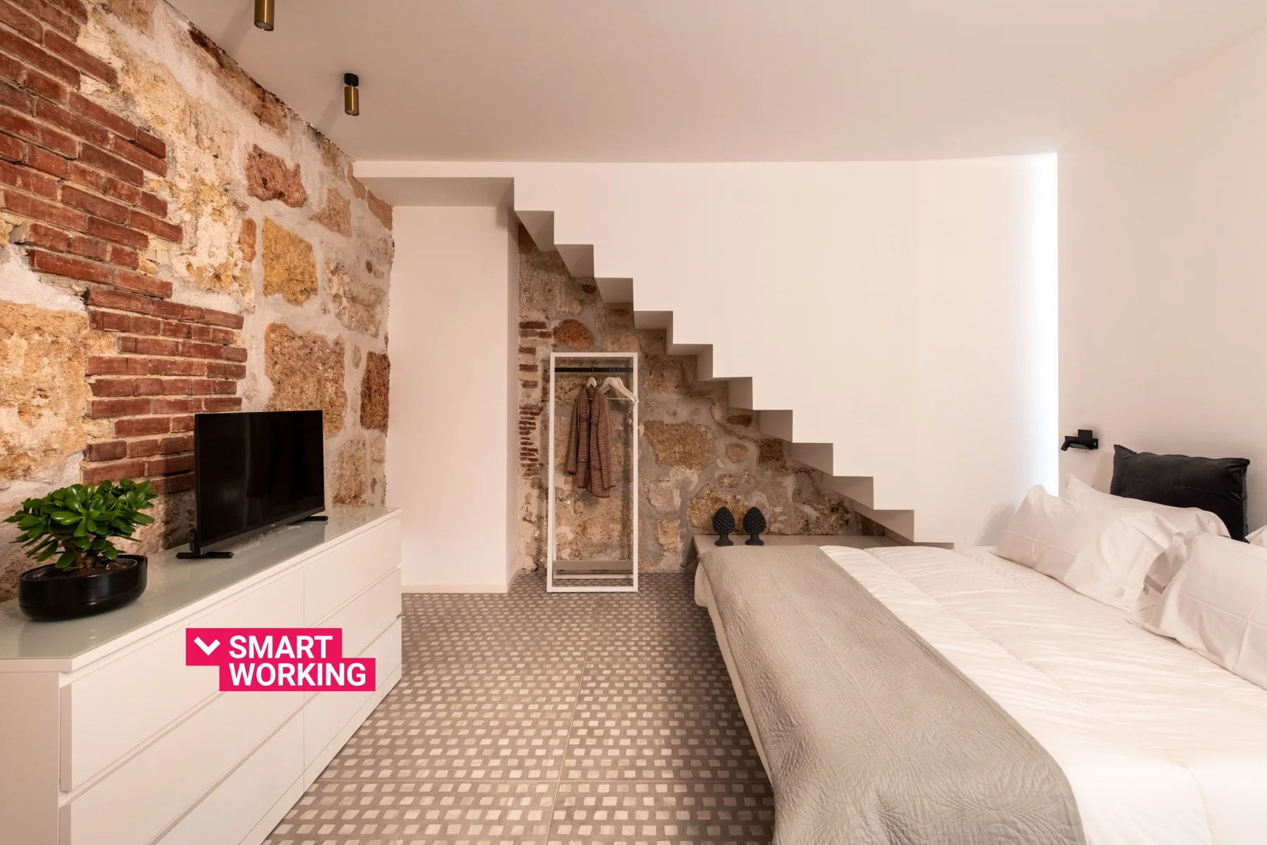A bedroom with a bed beside a staircase and an exposed brick wall.