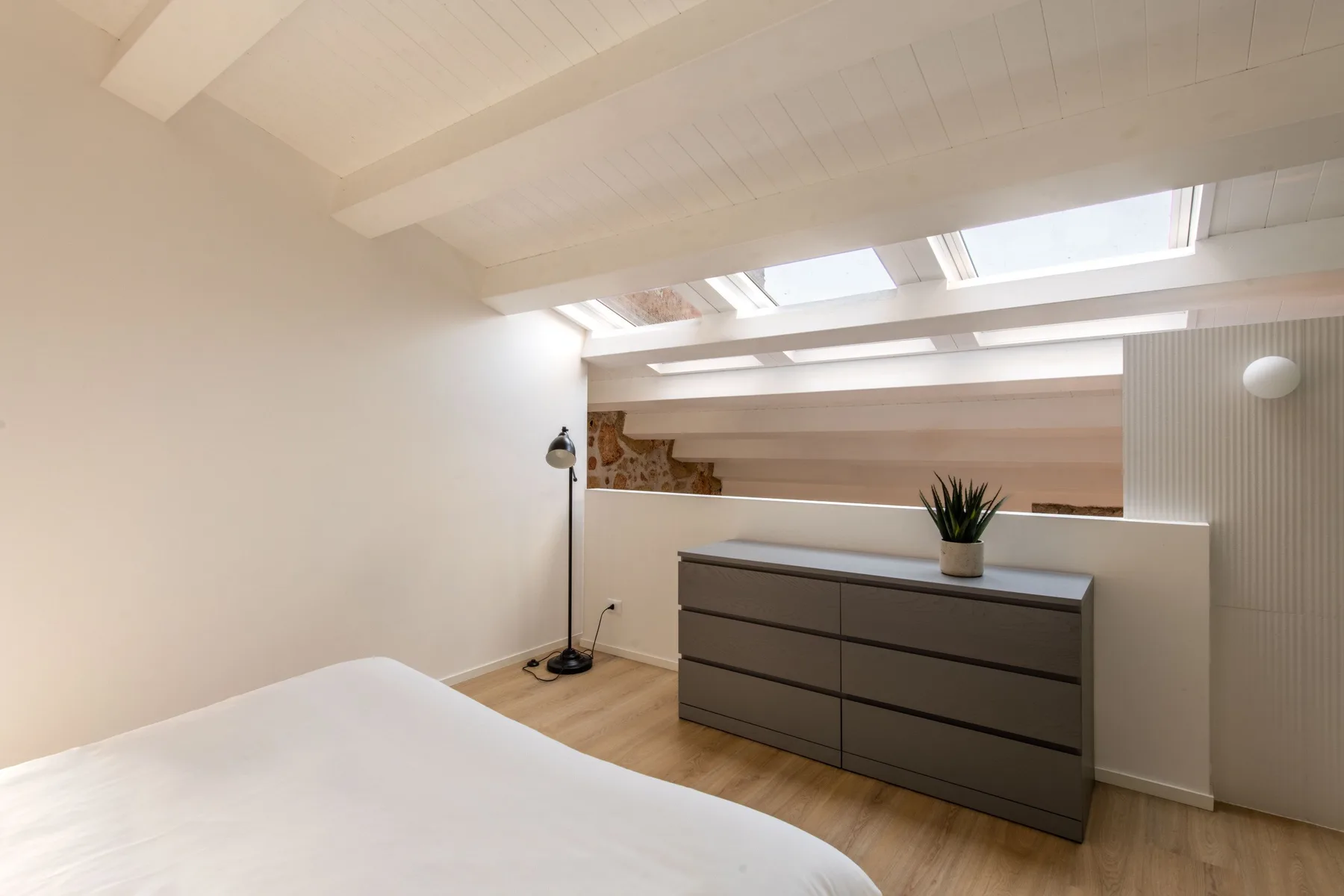 A bedroom with a bed, dresser, and skylights.