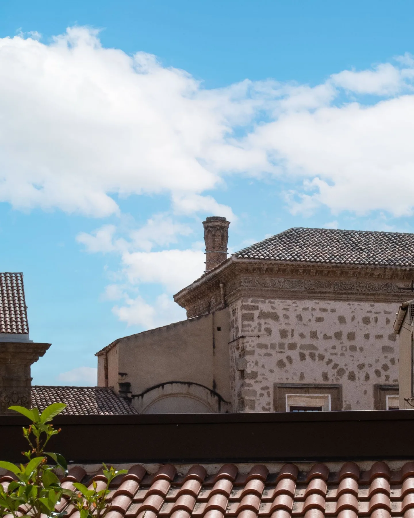 A historic stone building with tiled roofs stands beneath a partly cloudy sky.