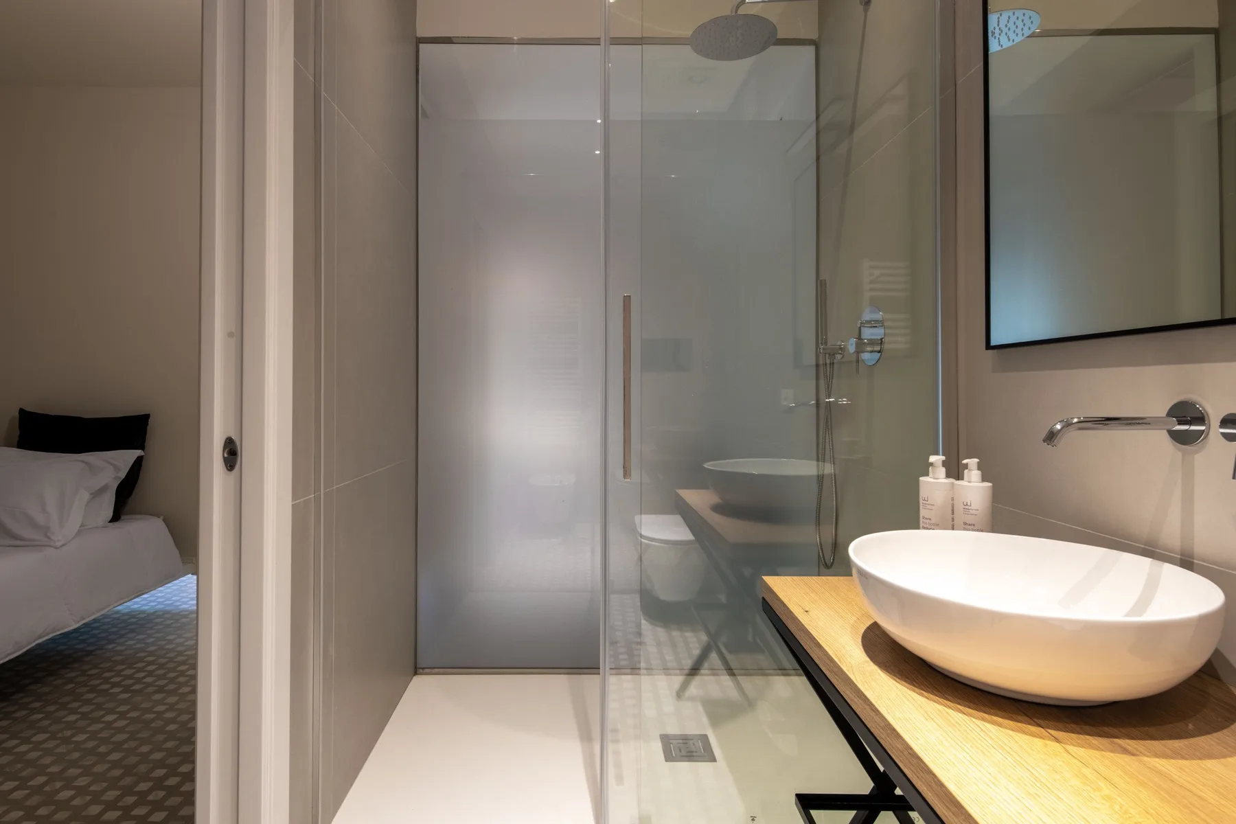 A bathroom with a glass shower and a white vessel sink on a wood vanity.