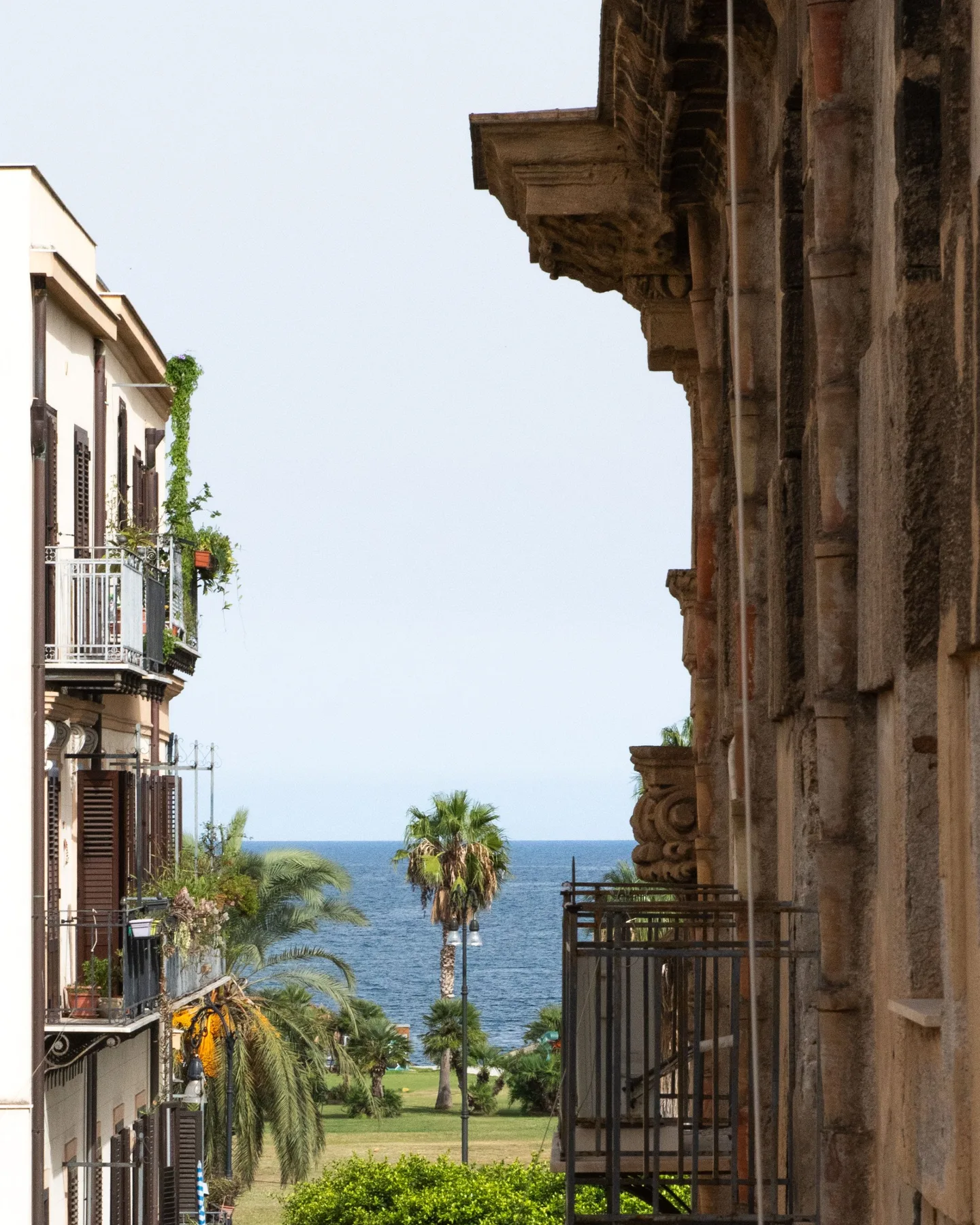 A narrow street opens toward the sea, with balconies and palm trees along the way.