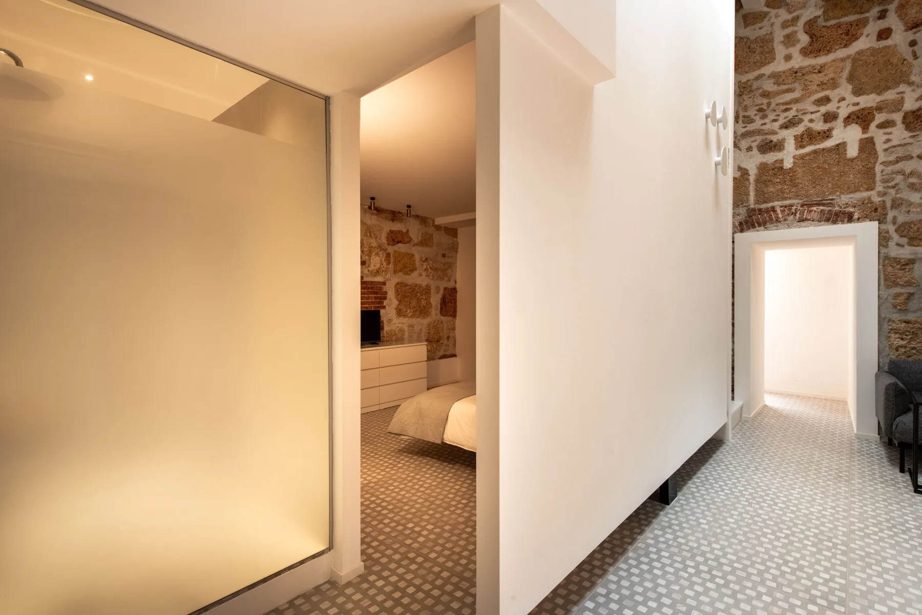 A bedroom doorway opens onto a tiled hallway with exposed stone walls.