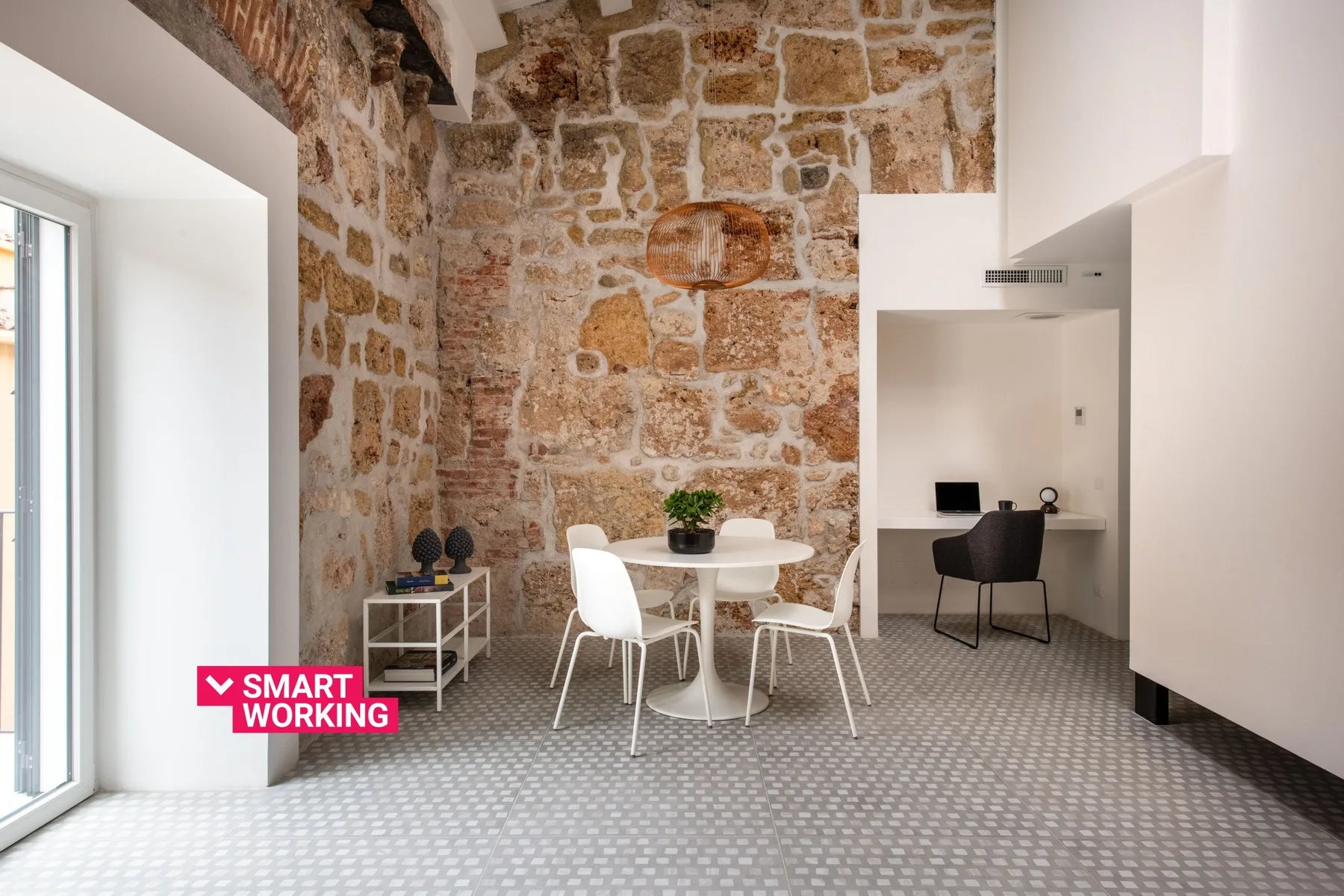 A bright room with exposed stone walls, a dining table, and a desk nook.