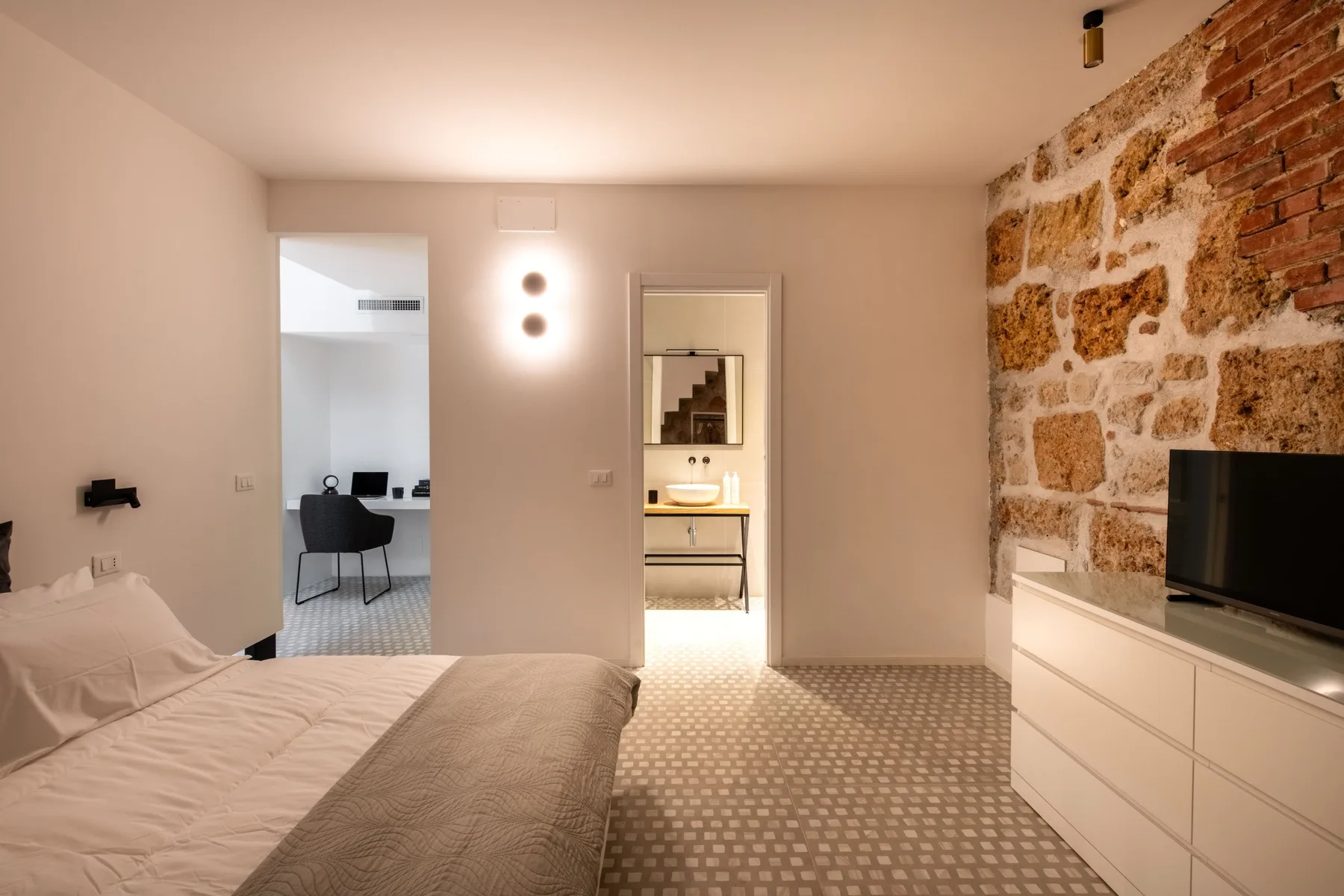 A bedroom with a bed, patterned floor, and exposed stone wall.