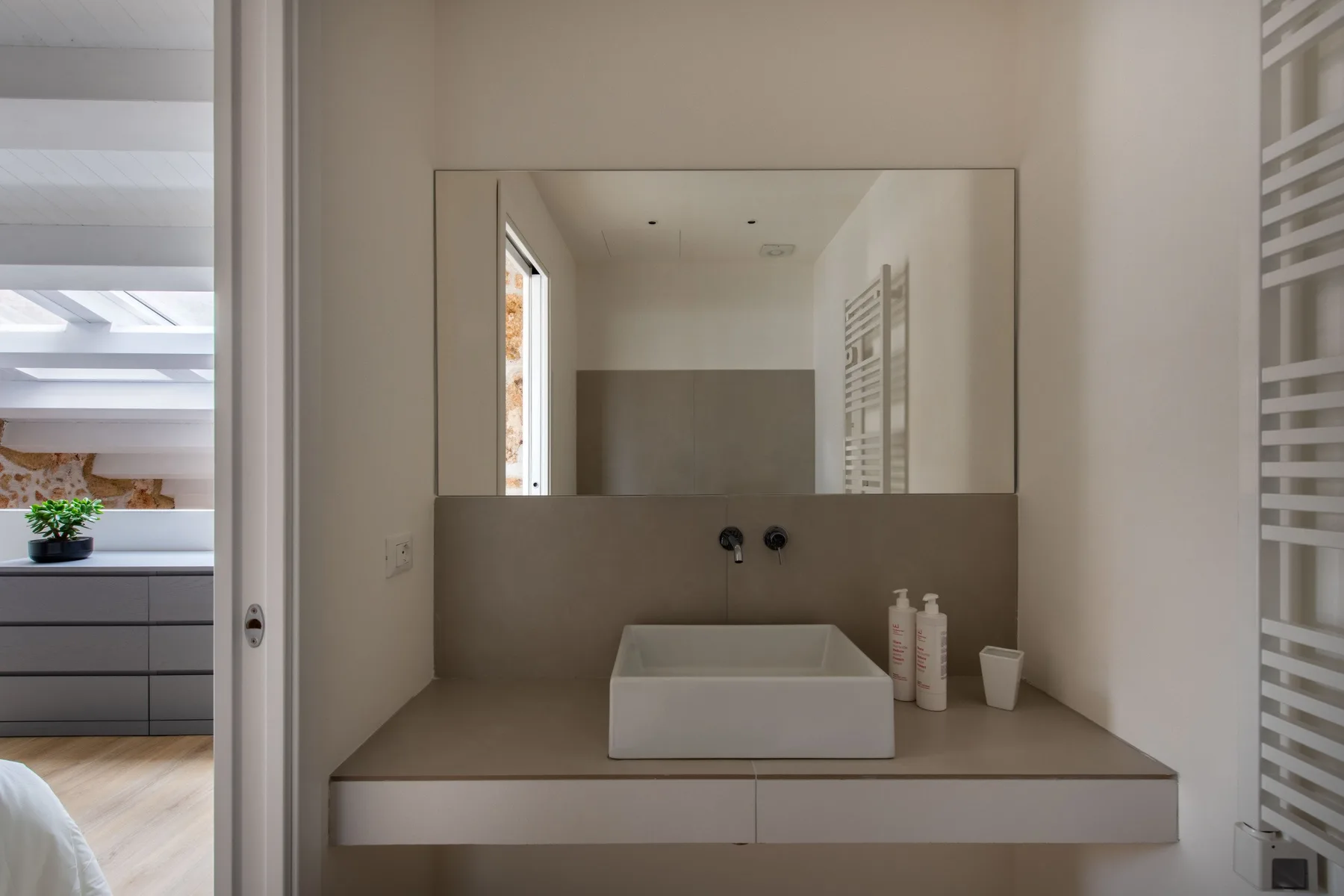 A bathroom vanity with a rectangular sink sits beneath a wide wall mirror.