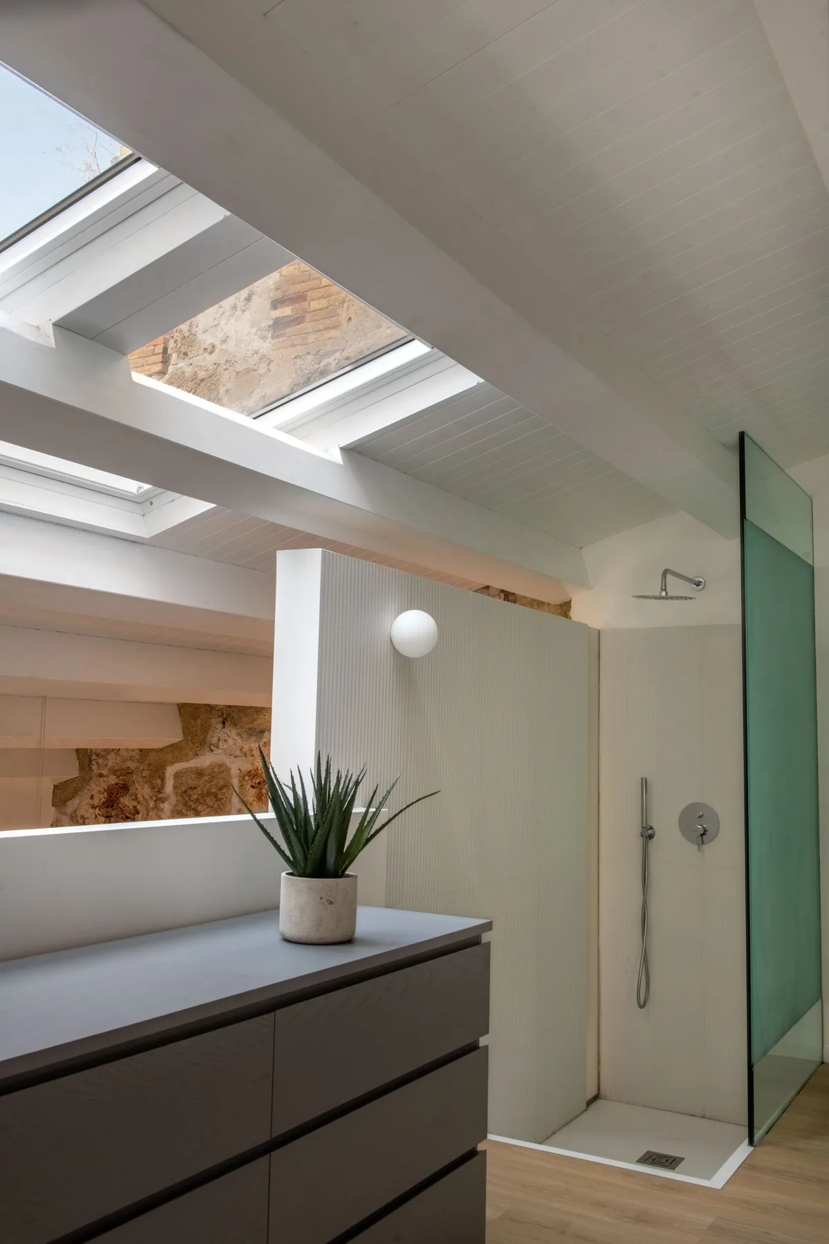 A bright bathroom with a vanity, potted plant, and open shower area.