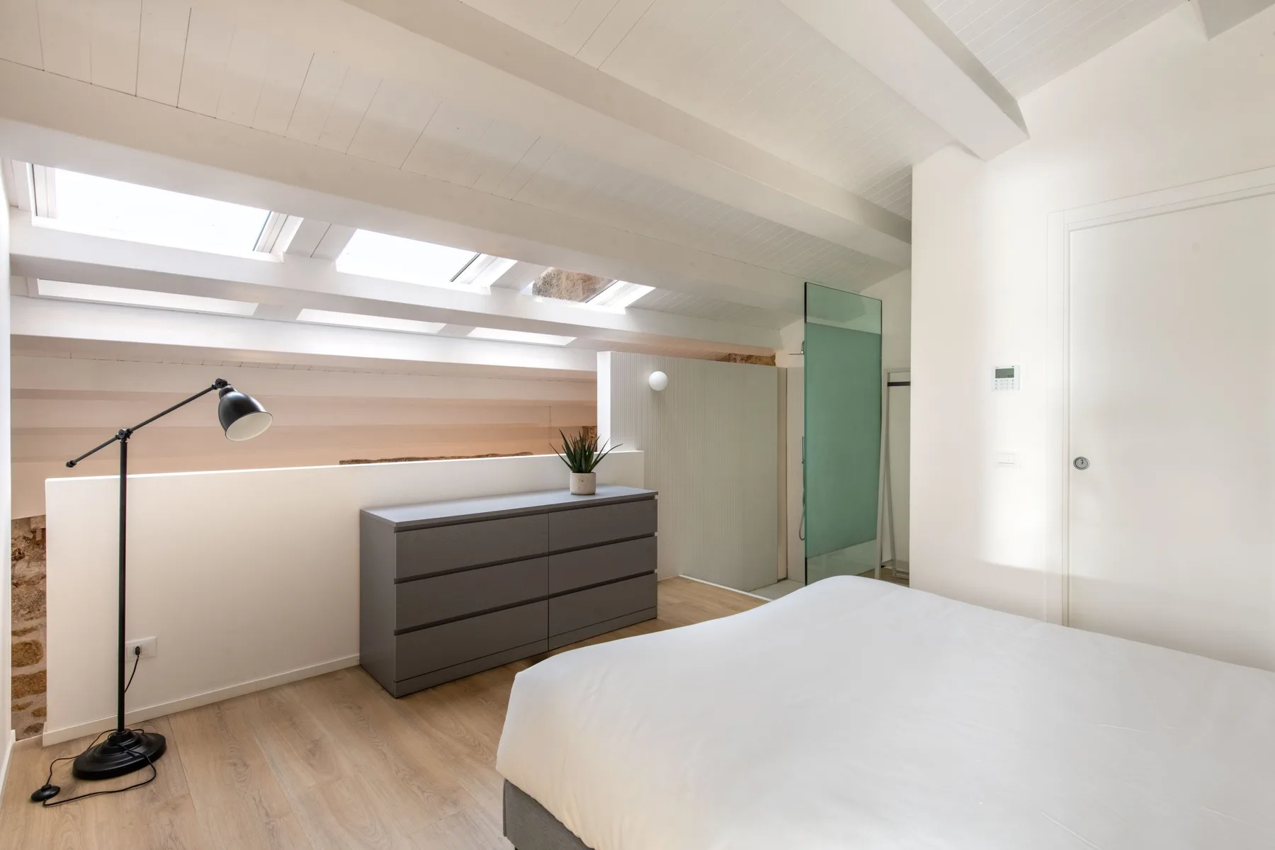 A bright bedroom with a bed, low dresser, and skylights.