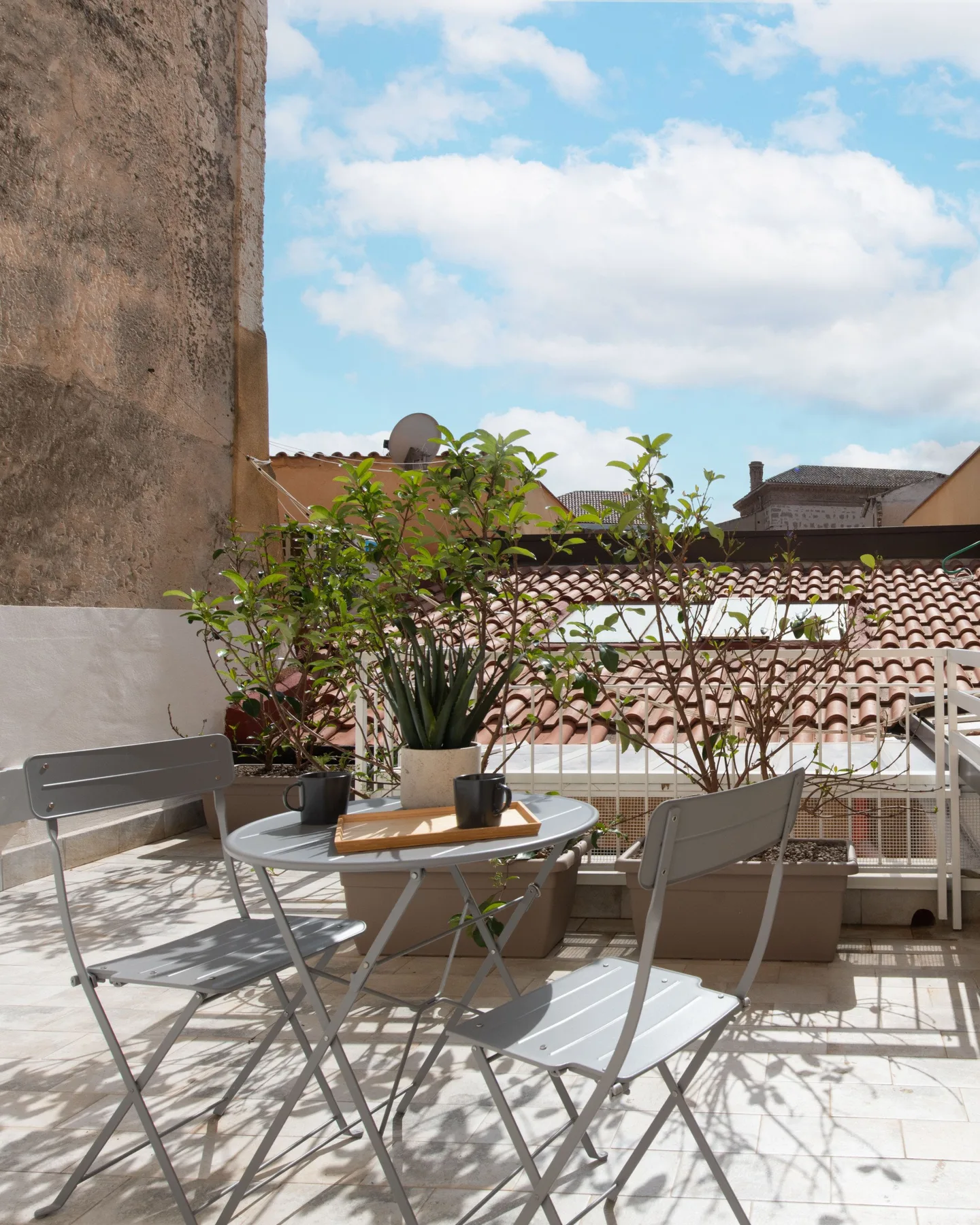 A sunny outdoor terrace with a small table, seating, and potted plants.