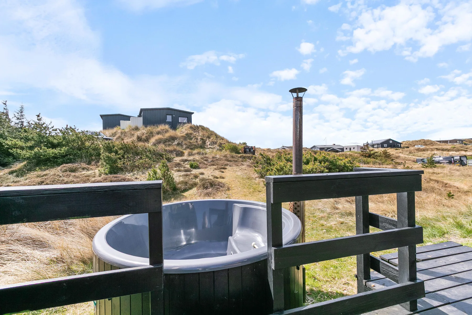 Una bañera de hidromasaje al aire libre está detrás de una barandilla de madera, frente a un paisaje arenoso.