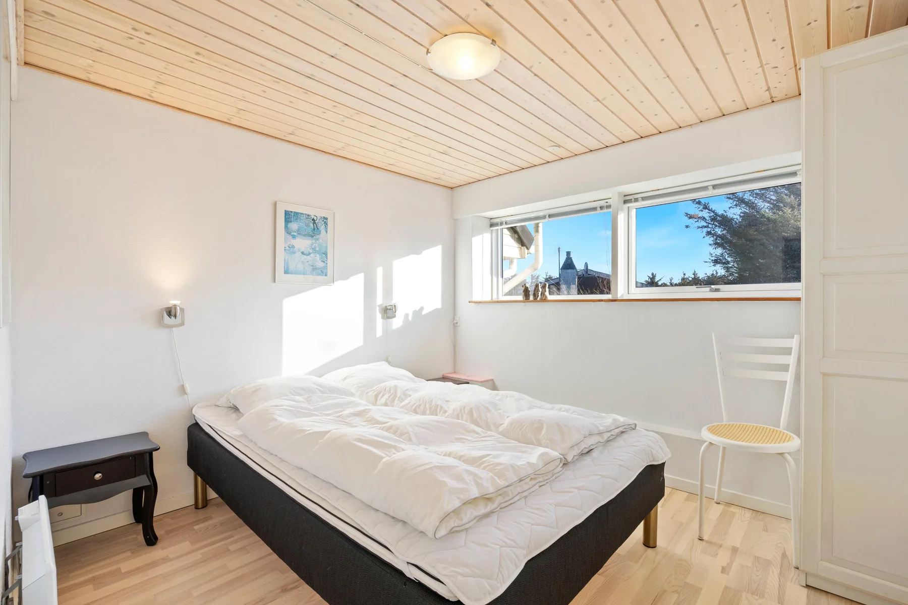 Un dormitorio luminoso con una cama doble bajo un techo revestido de madera.