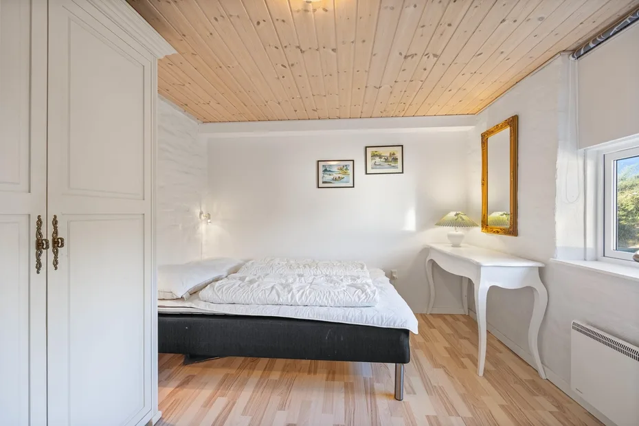 Un dormitorio luminoso con una cama y un escritorio junto a la ventana.