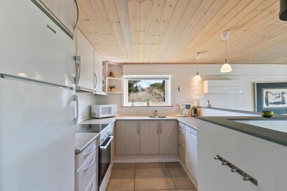Una cocina luminosa con muebles de madera clara, una ventana y suelo de baldosas.
