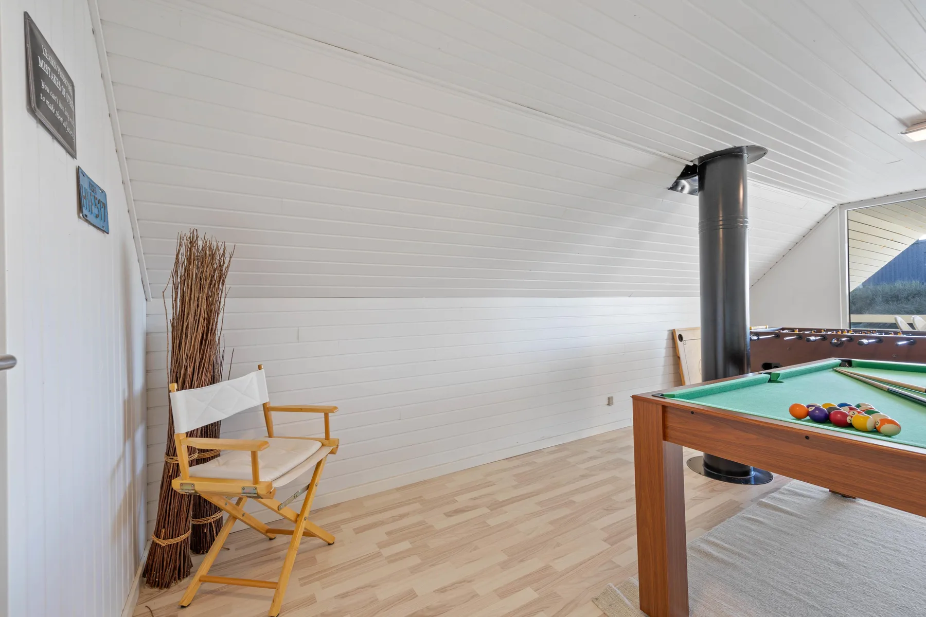 Una zona recreativa abuhardillada con una mesa de billar y una silla de madera.