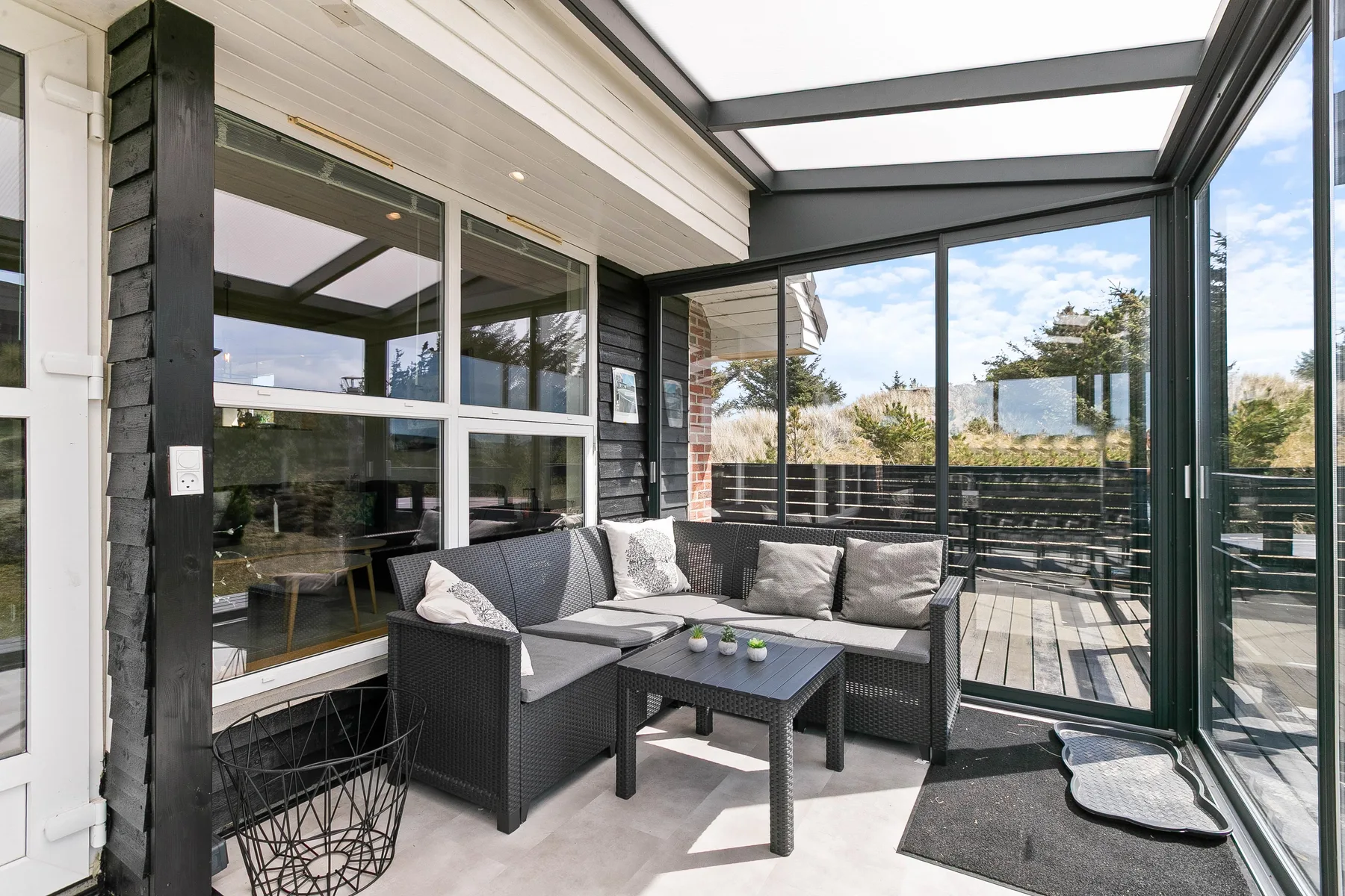 Un patio cubierto con asientos al aire libre y paredes de vidrio junto a una terraza.