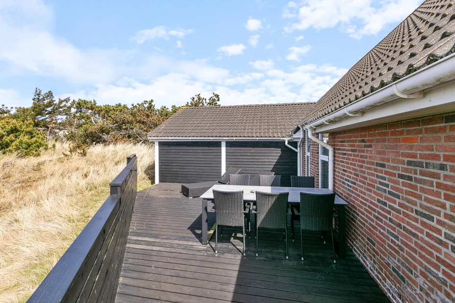 Una terraza exterior con una mesa de comedor y asientos junto a una pared de ladrillo.