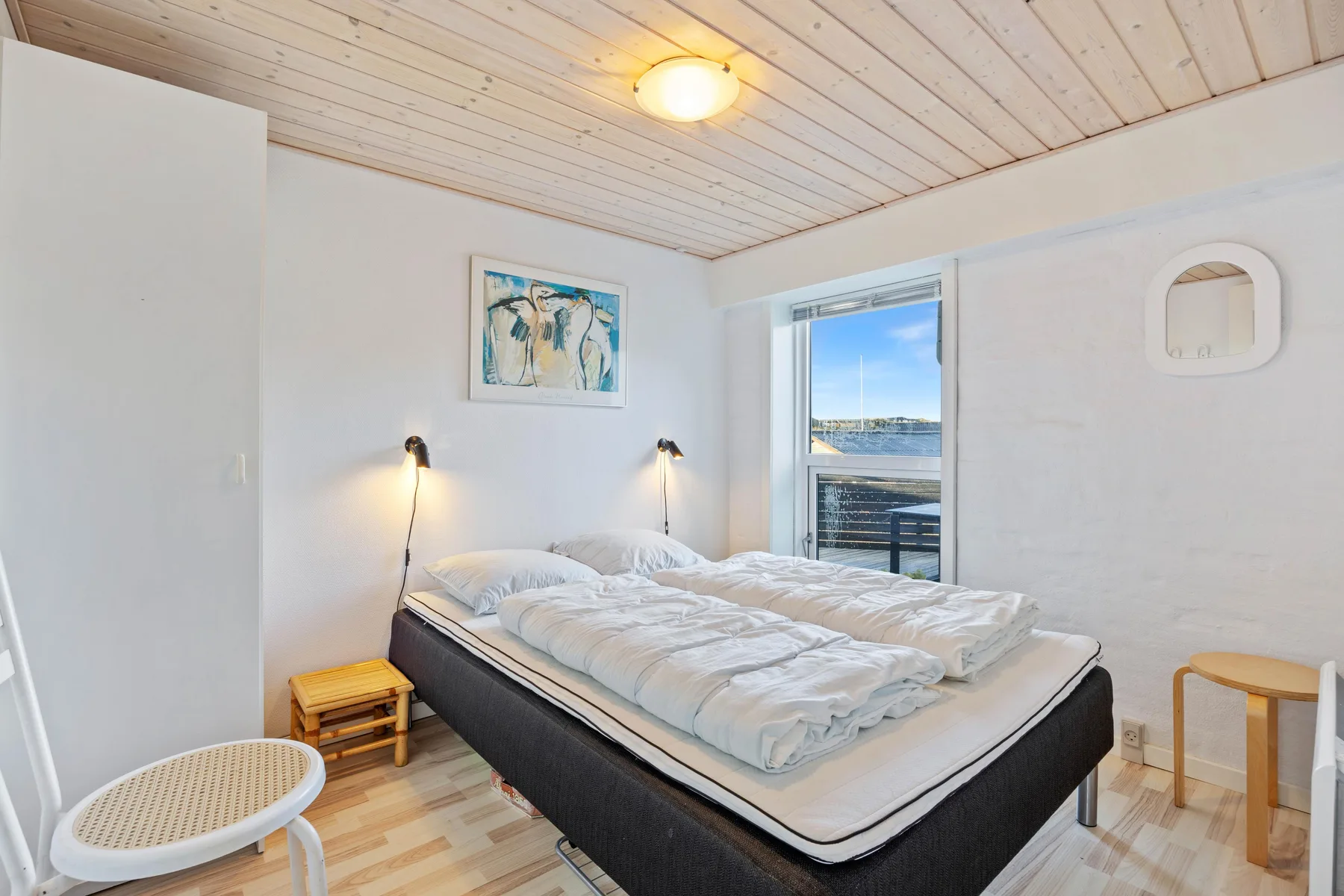 Un dormitorio luminoso con una cama doble y una ventana con vistas al agua.