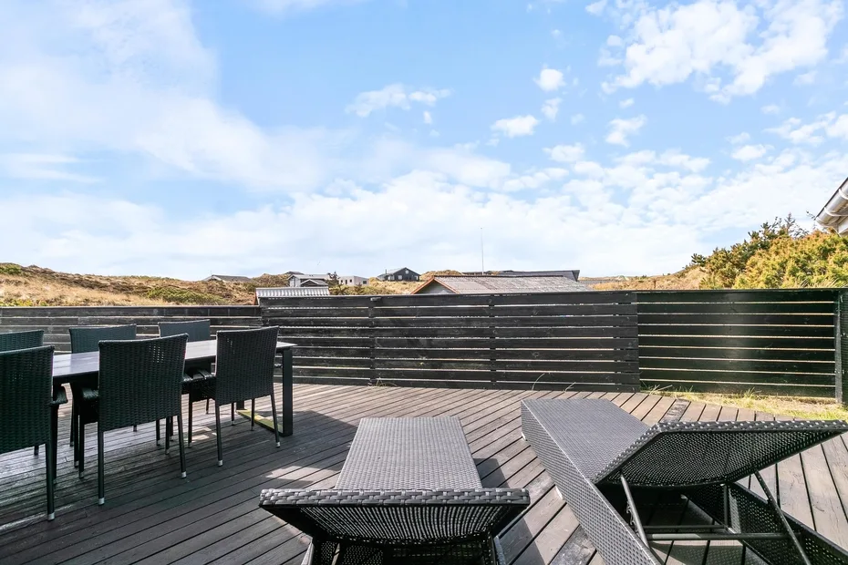 Una terraza exterior con asientos oscuros y una mesa da a un paisaje cercado.